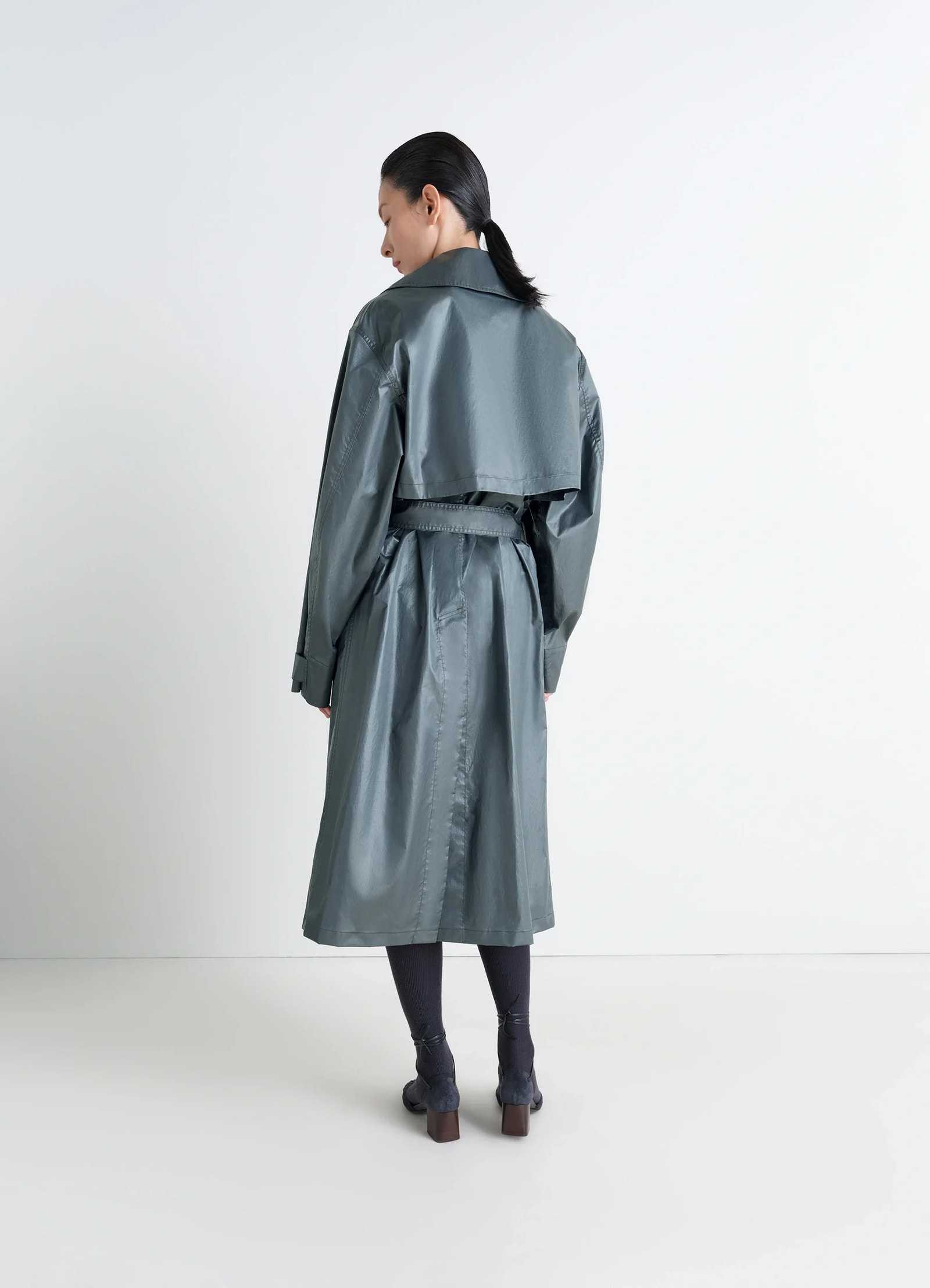 Oversized trench coat in metallic coated cotton, model shot, back view vented hem, storm flap