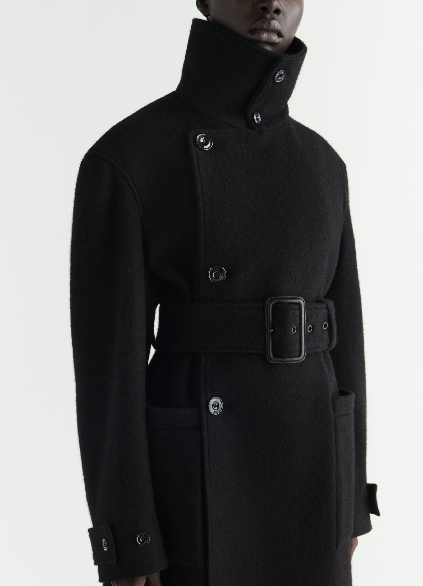 Fitted black felted wool and alpaca blend coat with high collar and belt worn by model lemaire