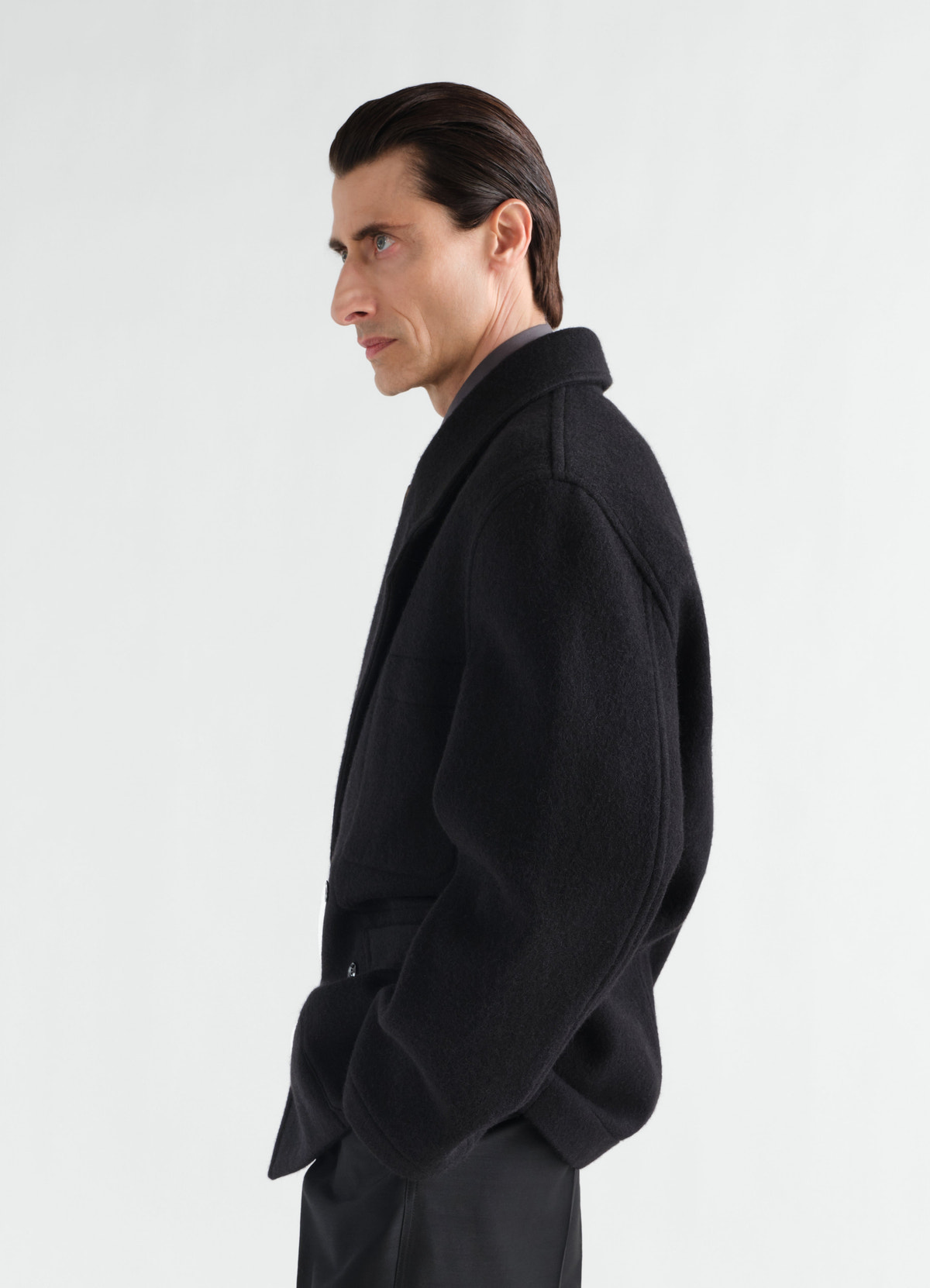 Manteau court à double boutonnage en mélange de laine et alpaga feutré, coloris noir, porté par un mannequin, vue de profil