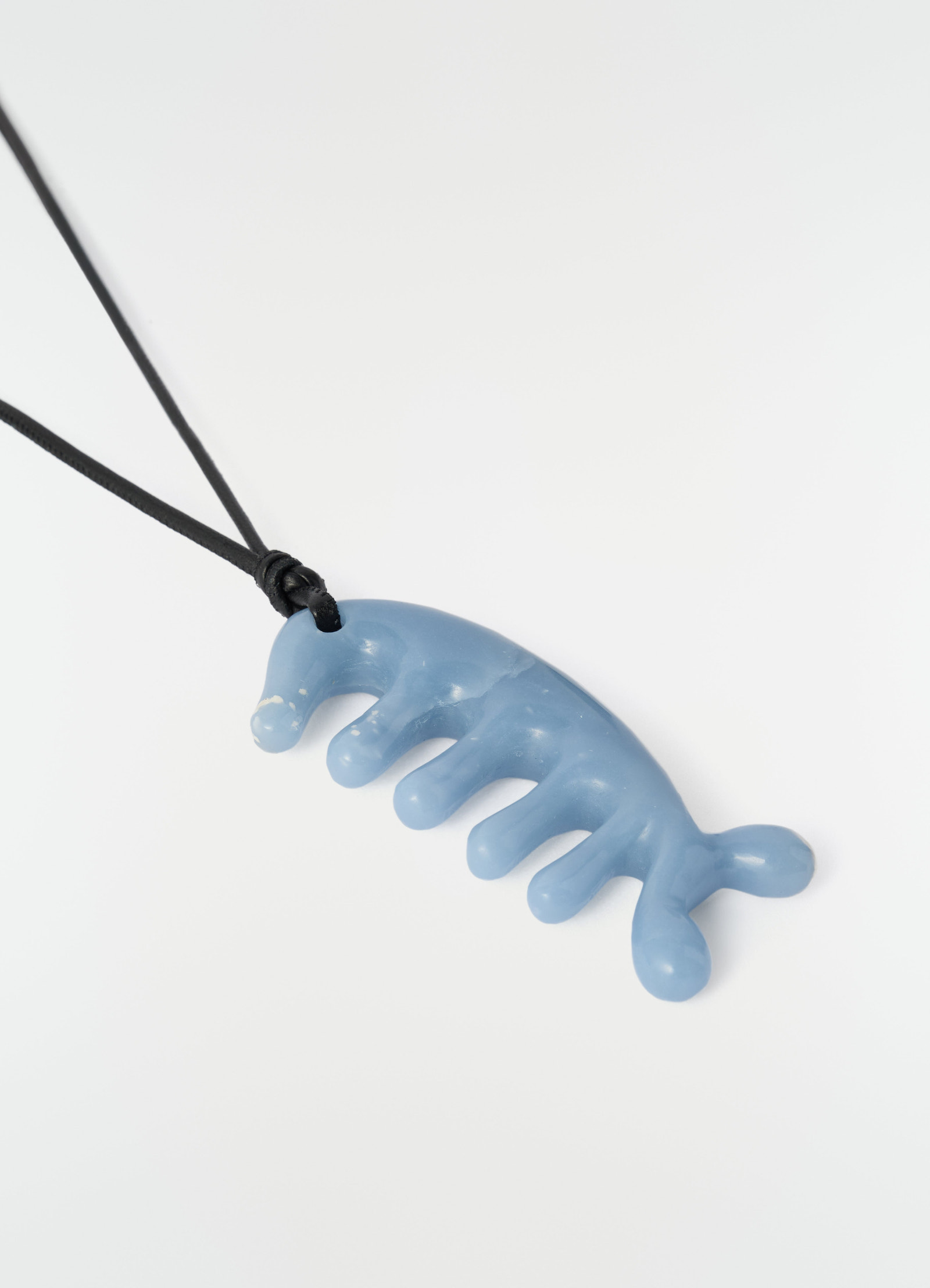 Beluga gua sha necklace in blue angelite resin with black cord lemaire plain white background close-up detail
