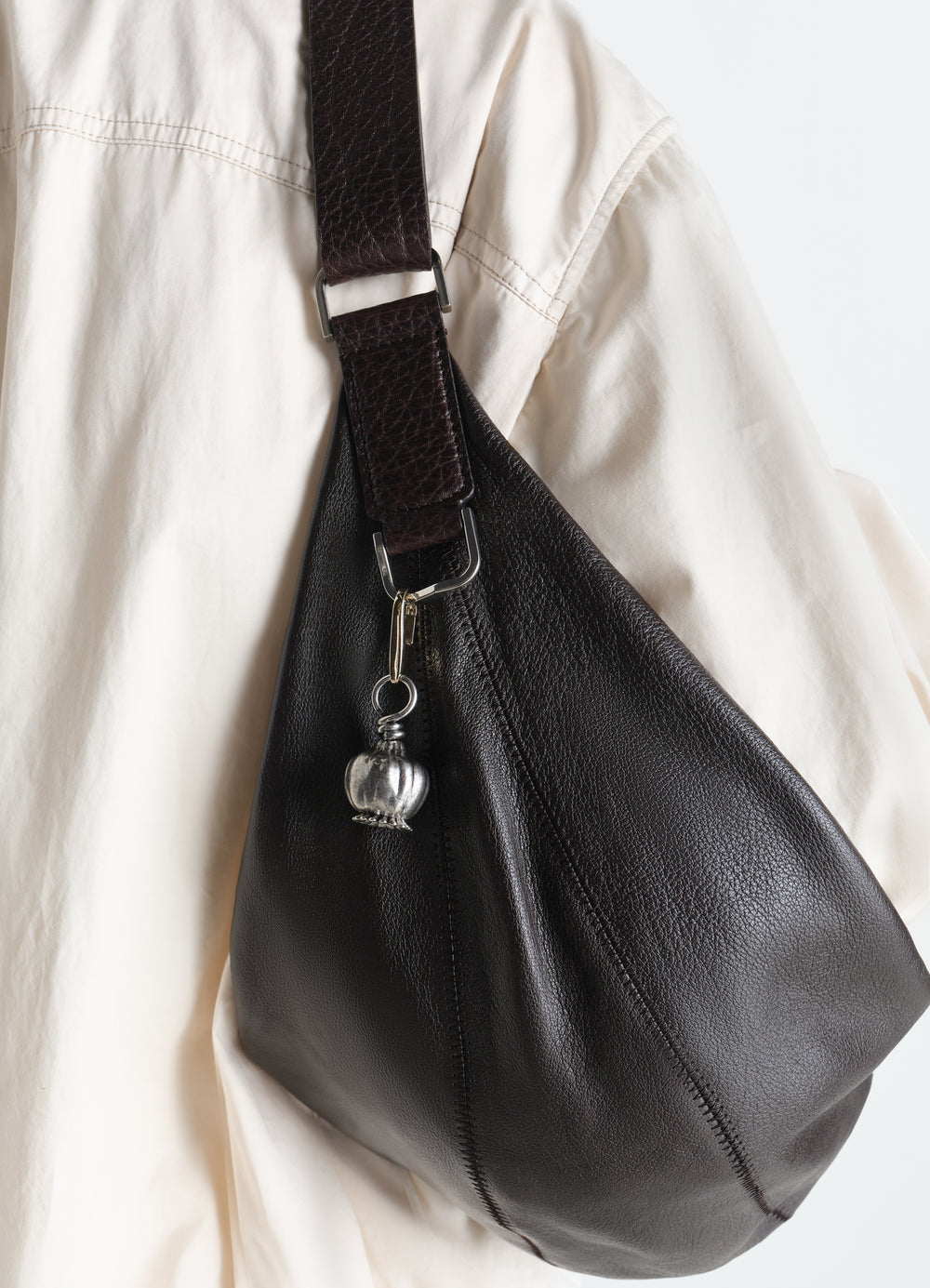 Maxi Thistle bag charm silver metal detail hanging on black leather LEMAIRE bag worn by model
