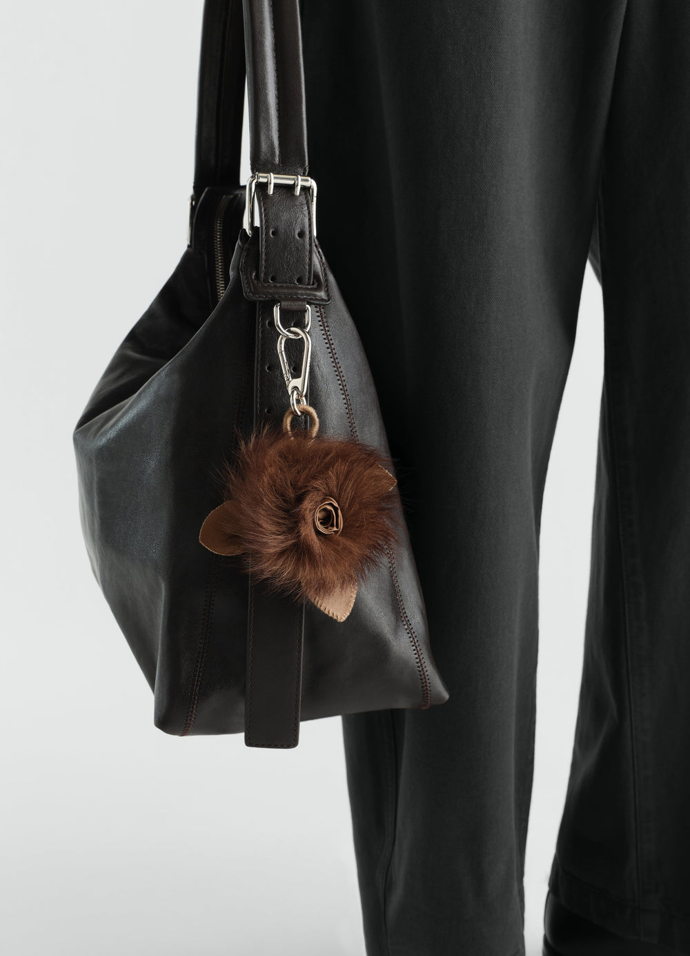Fuzzy brown rose charm in lambskin shearling on black leather bag worn by model LEMAIRE styled look