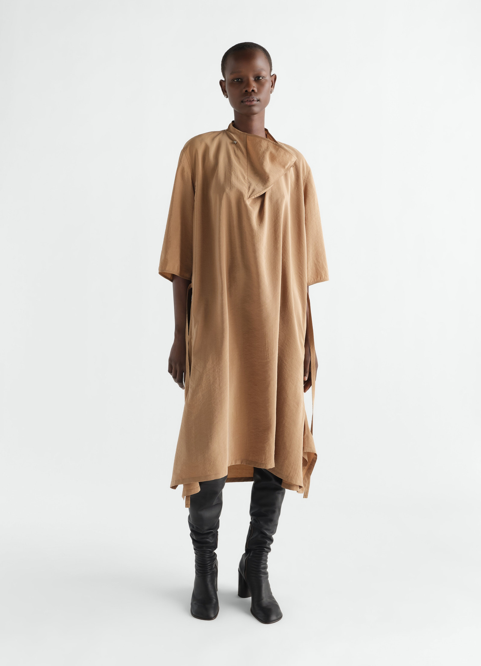 Soft-collar camel dry silk dress by lemaire worn by model with black leather knee boots front view