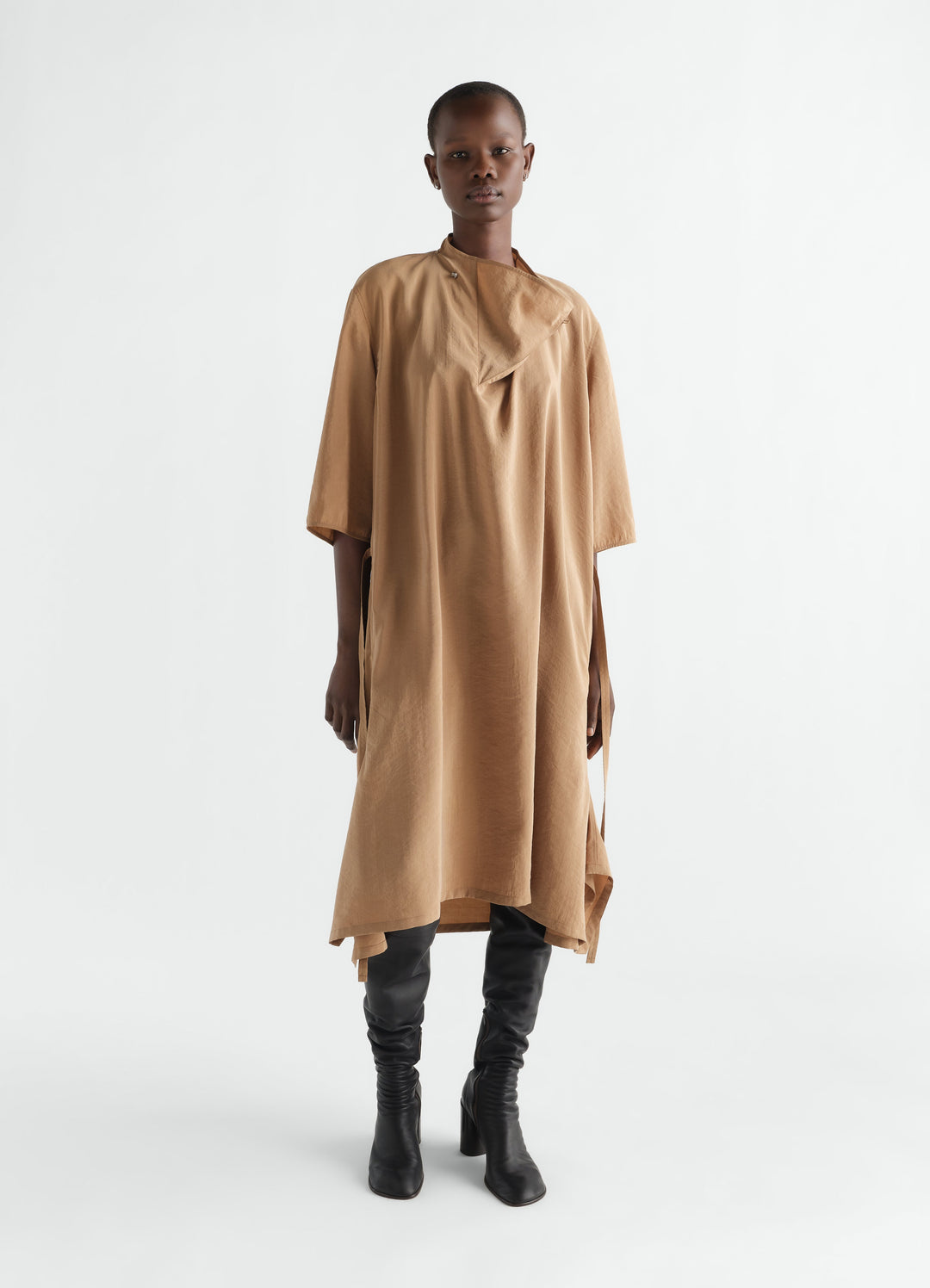 Soft-collar camel dry silk dress by LEMAIRE worn by model with black leather knee boots front view