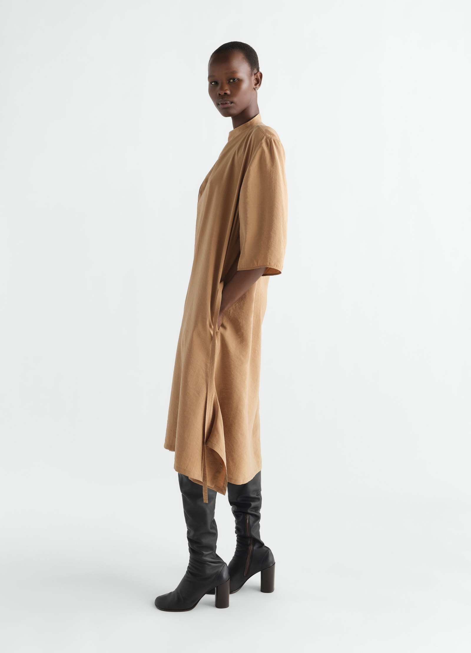 Soft-collar camel dry silk dress by lemaire worn by model side view with black leather boots