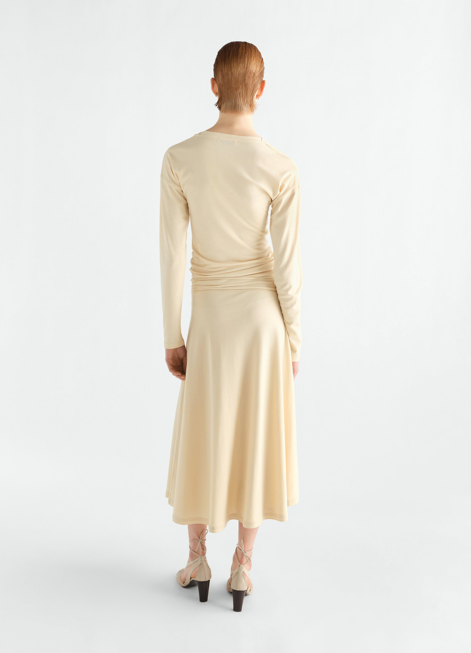 Fluid long-sleeve cream silky jersey crepe dress by lemaire worn by a model shown from back on white background