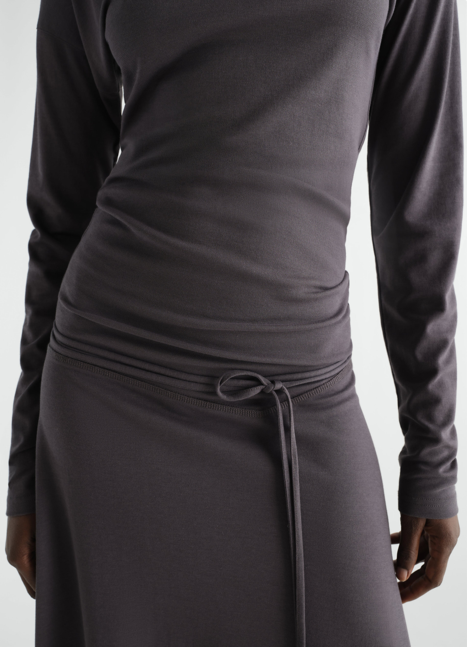 Fluid long-sleeve dress in silky dark grey jersey crepe with waist tie detail worn by model lemaire