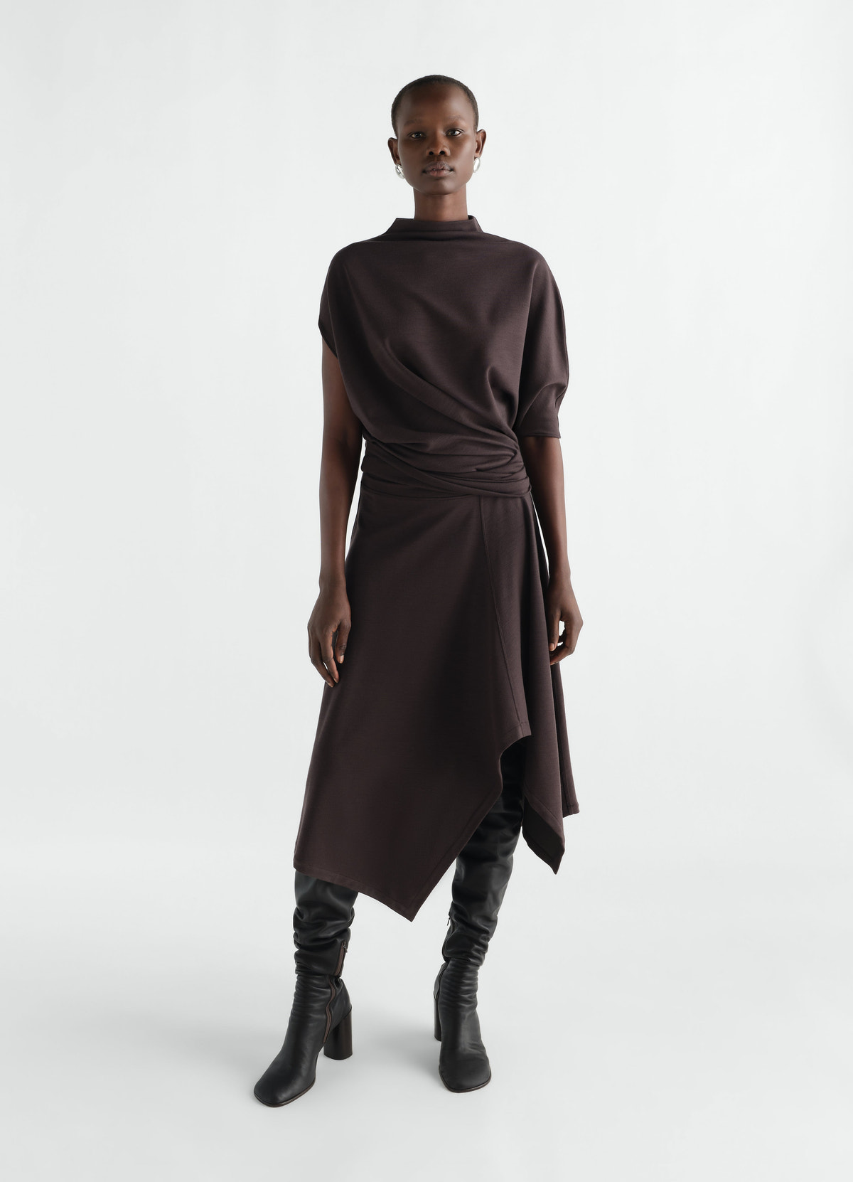 Twisted wool-blend jersey dress in dark brown by lemaire worn by model with asymmetric hem and high boots