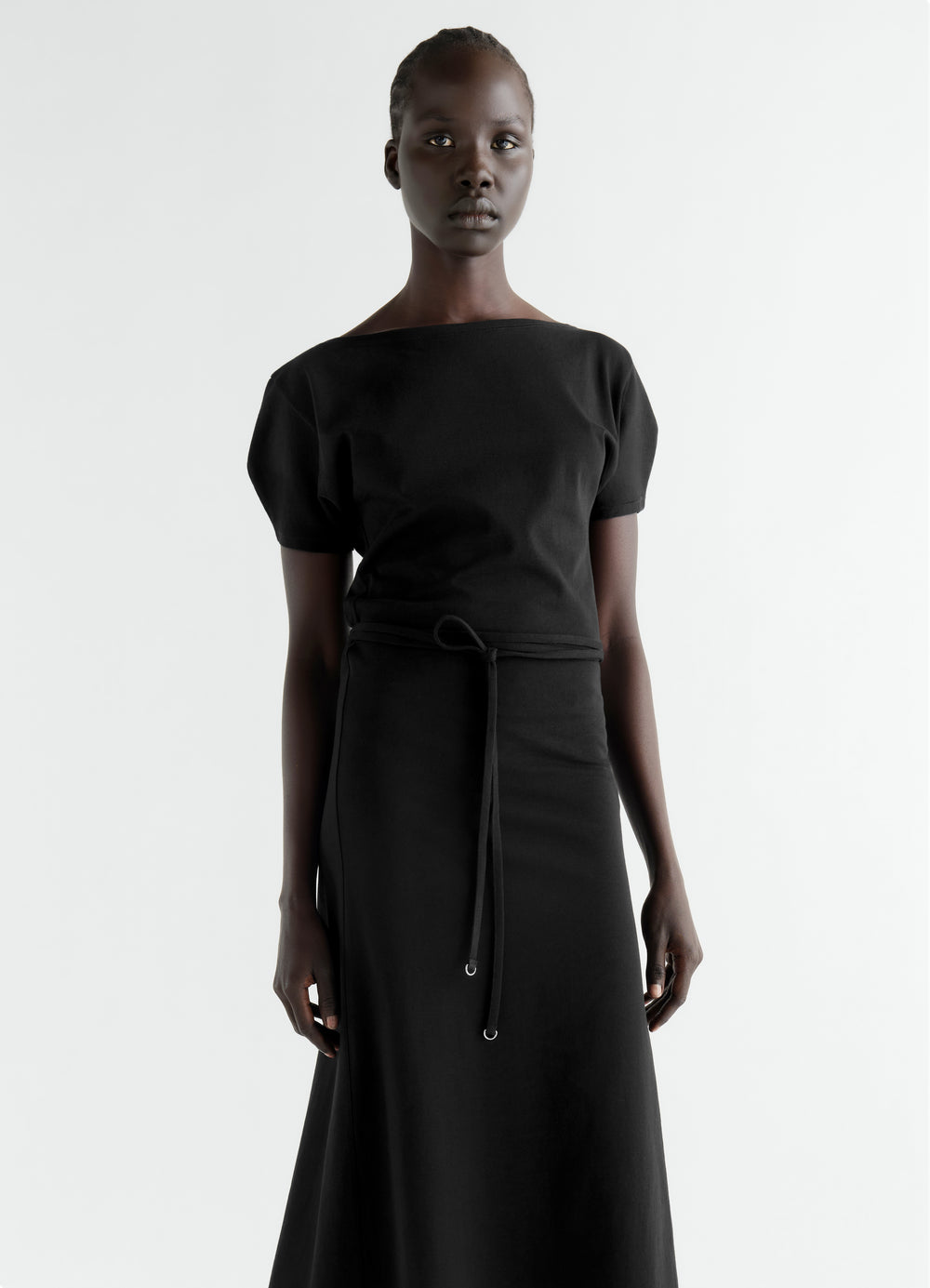 Belted black heavy cotton jersey dress by LEMAIRE worn by model with short sleeves and boat neckline front view