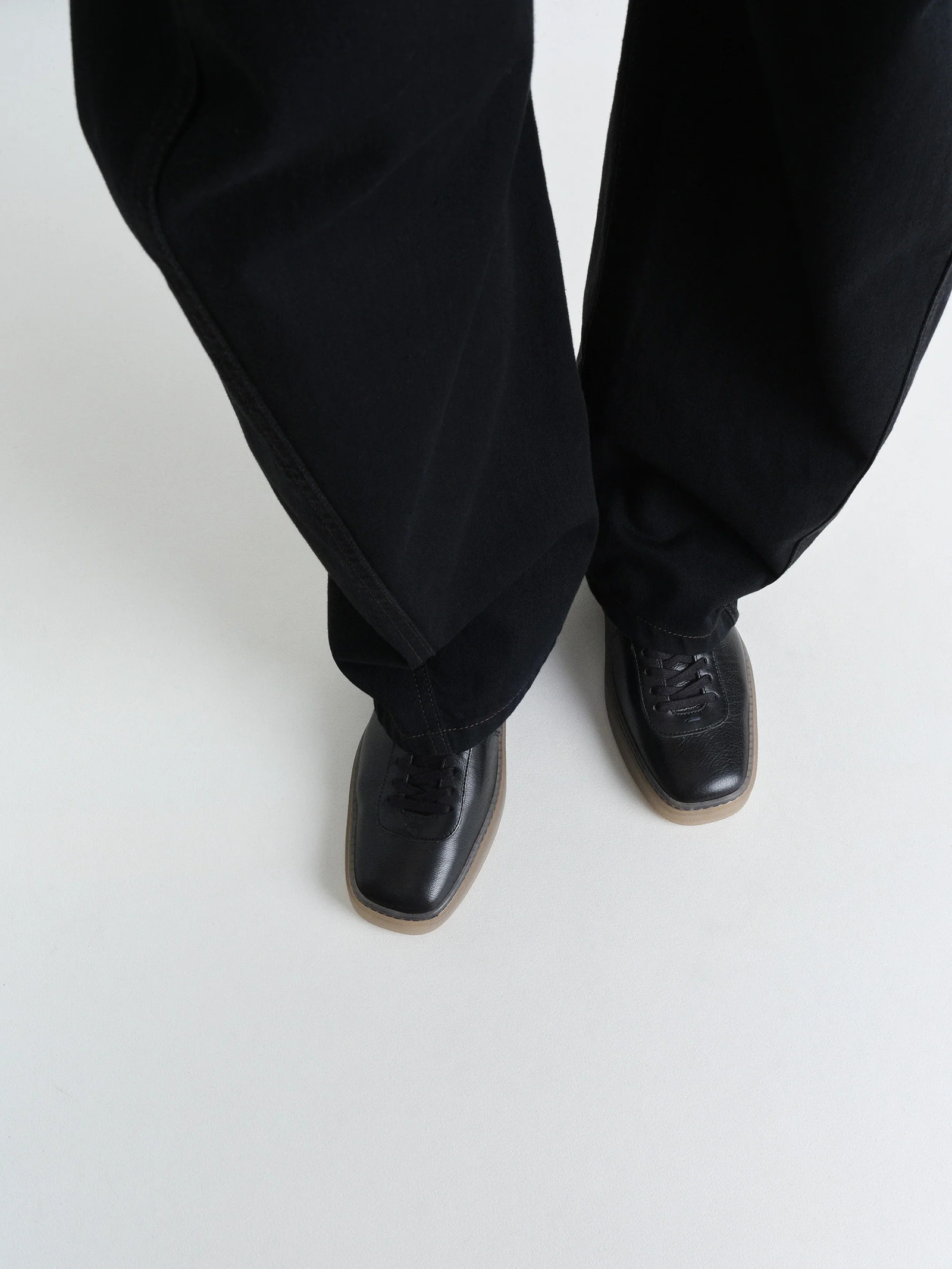 Linoleum laced up trainers in black smooth cow leather, model shot, top down view contrast sole detail