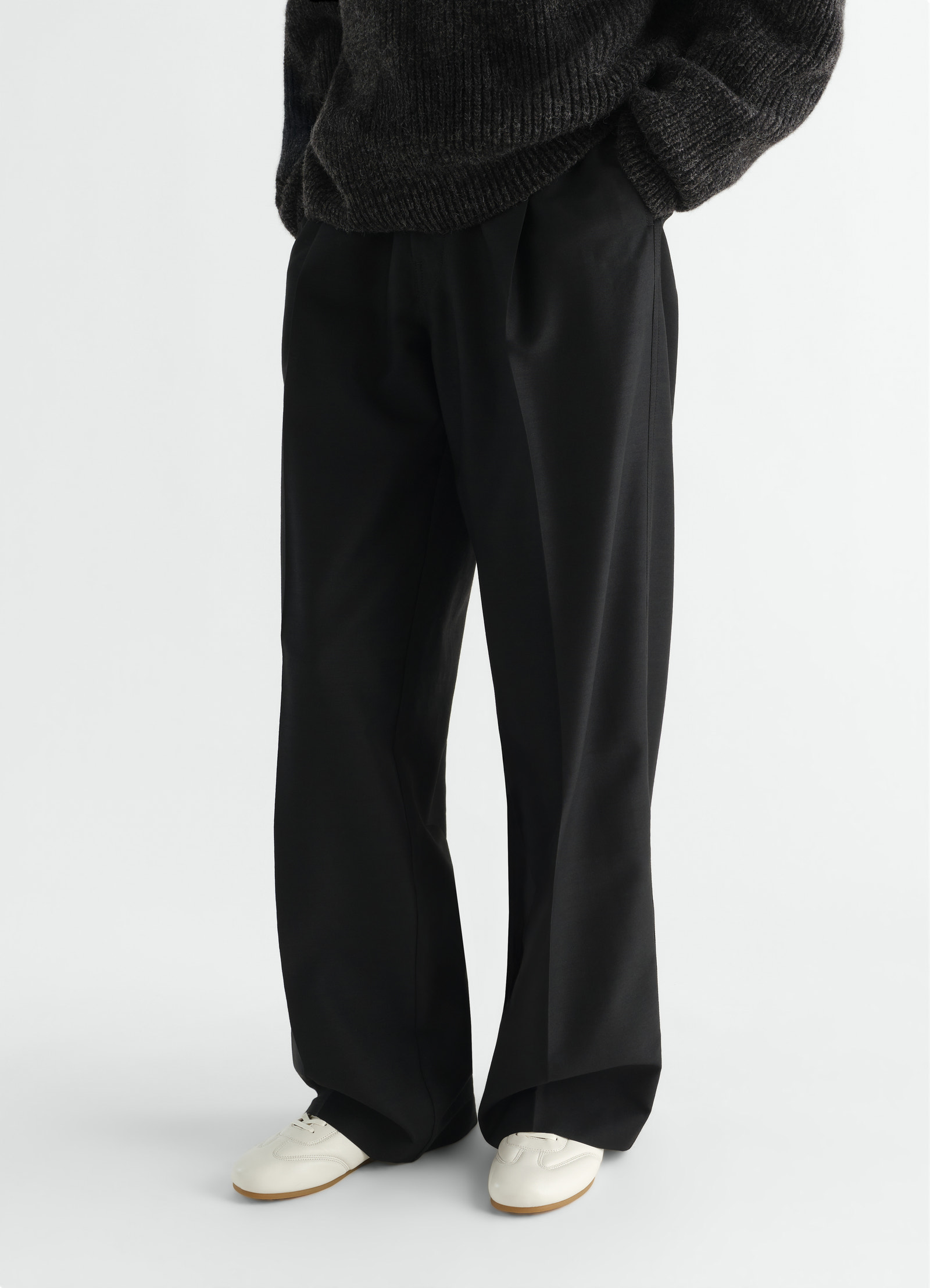 Soft black leather soft runner shoes by lemaire worn by model with black trousers front view