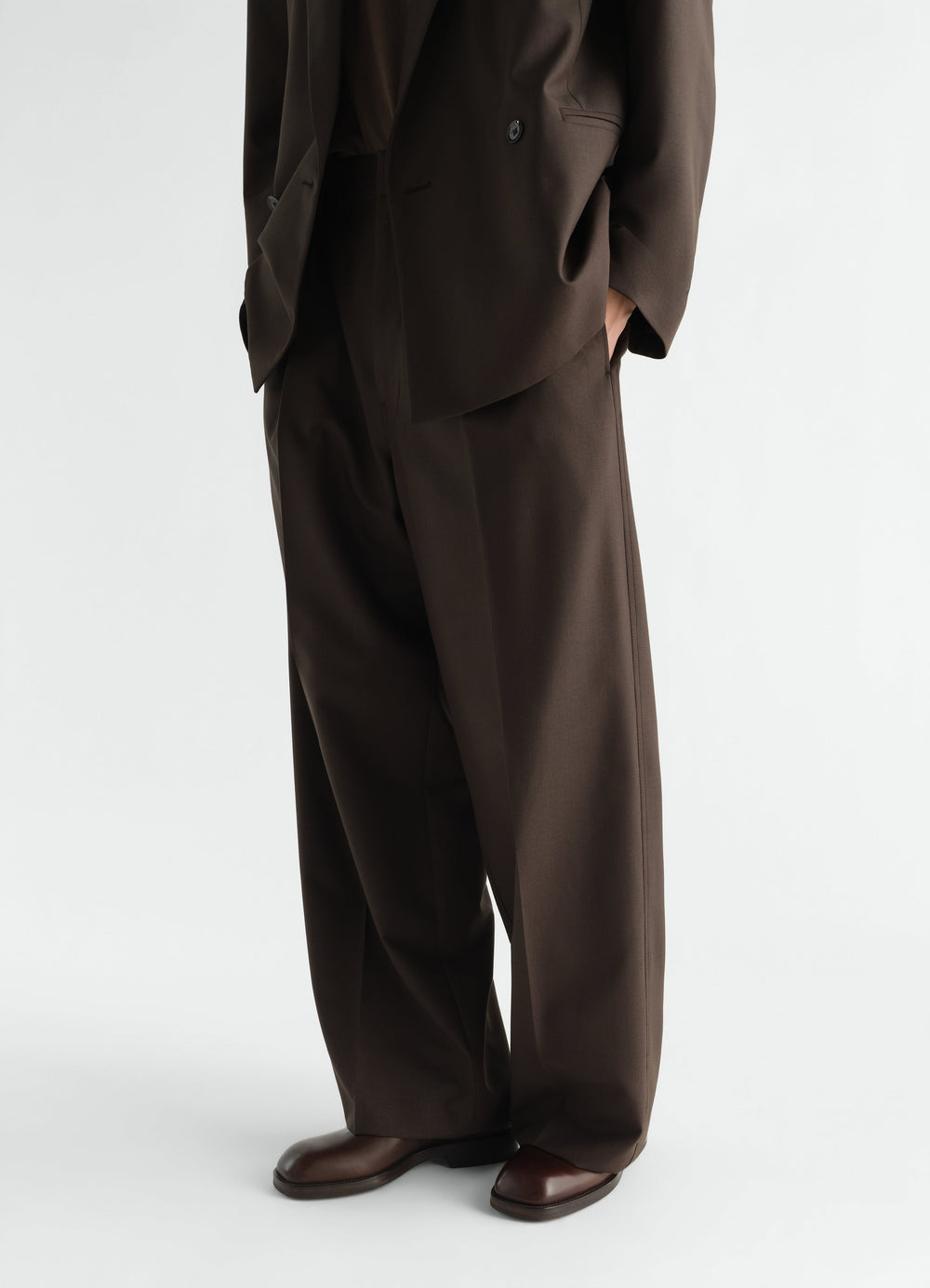 Zipped ankle boots in shiny brown leather by LEMAIRE worn by model, side view with matching trousers