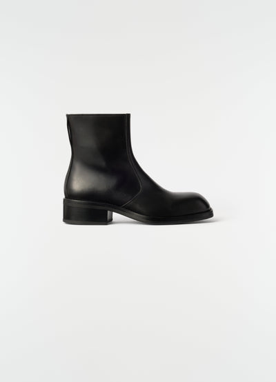 Zipped ankle boots in shiny black leather by LEMAIRE side view on plain white background