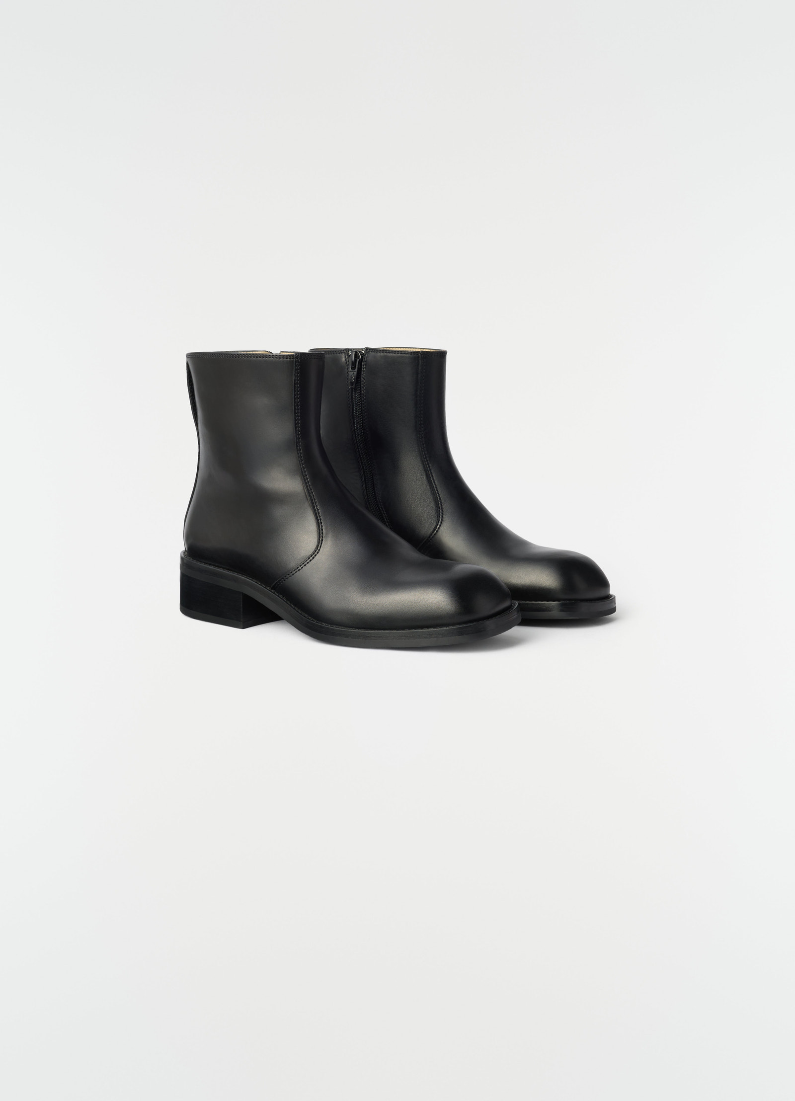 Zipped black shiny leather ankle boots lemaire styled side view on plain white background