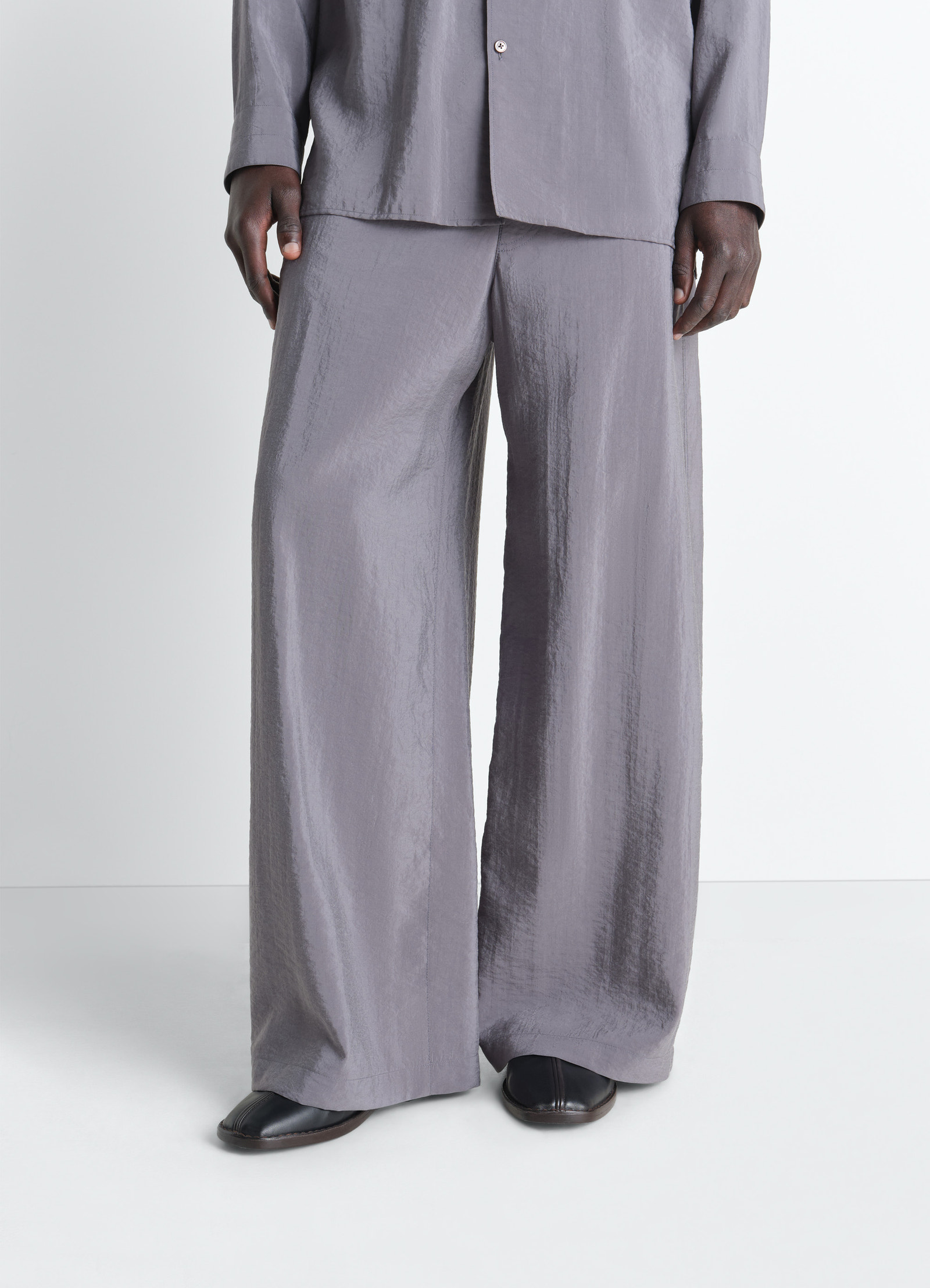 Lemaire flat piped slippers in black nappa lamb leather, model shot, bottom view shiny texture, under pants