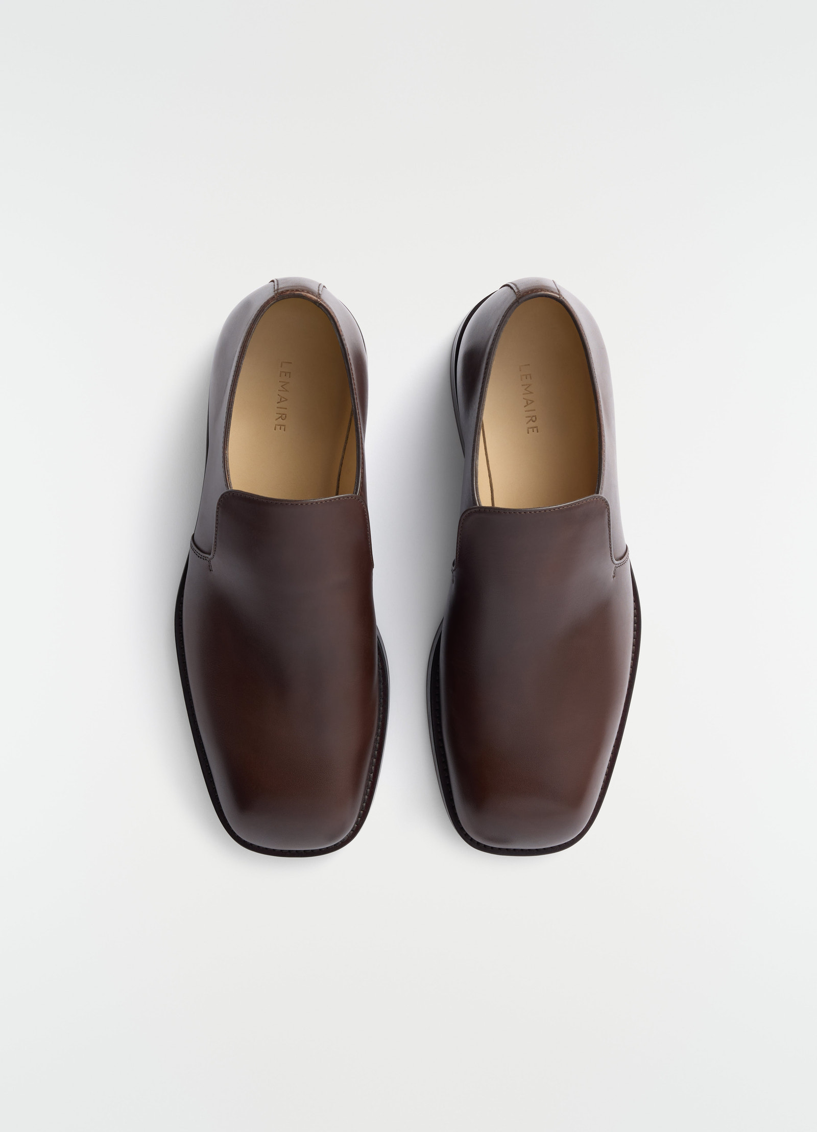 Brown shiny leather formal loafers lemaire close-up top view on plain white background