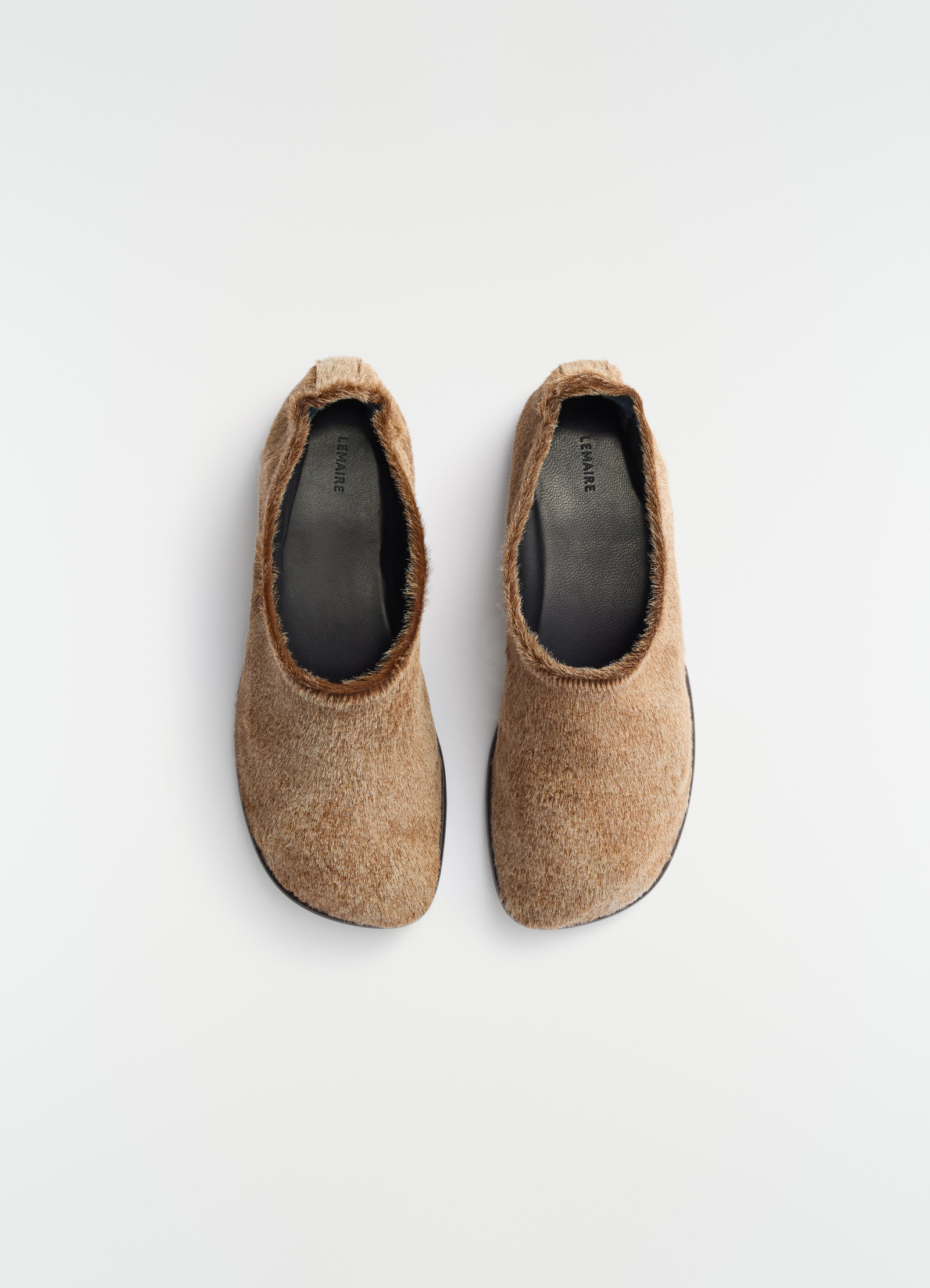 Glove slip-ons in natural brown pony-style leather with black insoles by lemaire top view plain white background