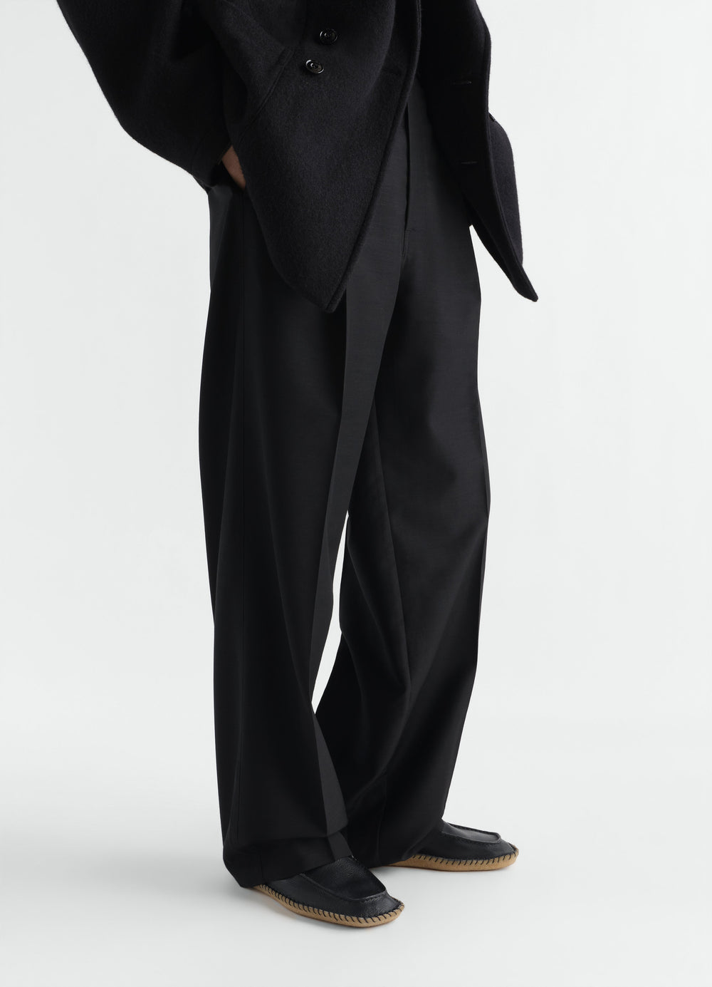 Desert moccasins in black vegetable-tanned leather by LEMAIRE worn by model, side view on white background