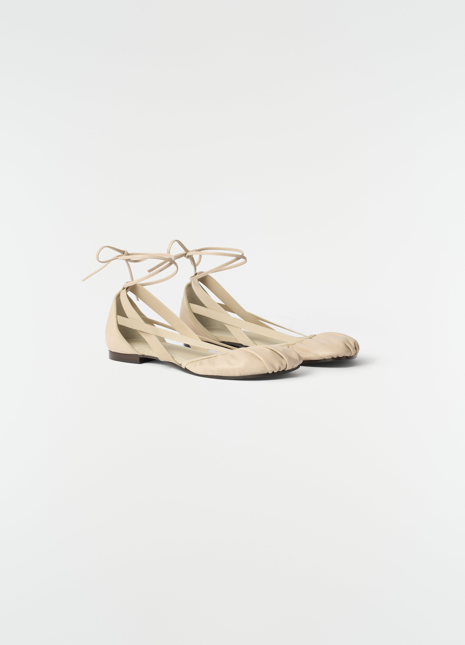 Flat pedille ballerinas in beige goat leather by lemaire styled on plain white background with ankle ties visible