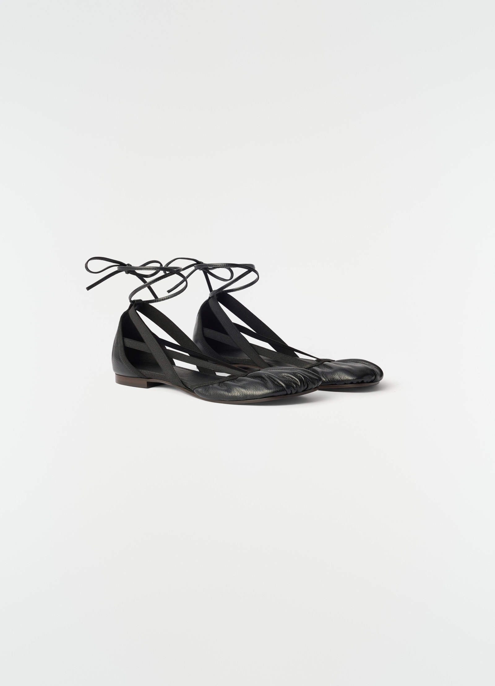 Flat pedille goat leather ballerinas in black with ankle ties styled on plain white background lemaire