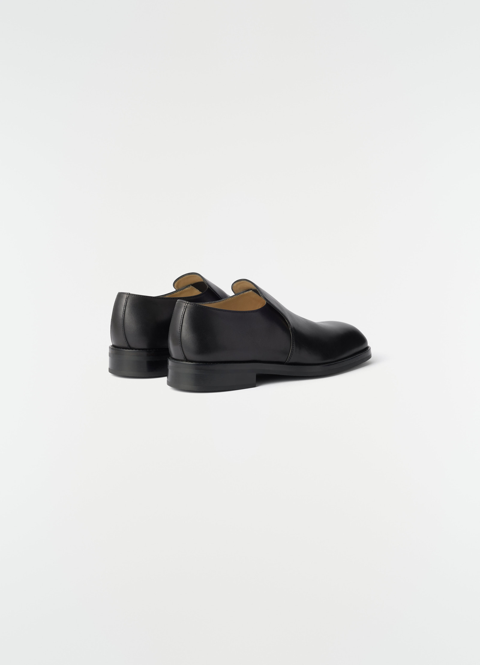 Formal black shiny leather loafers by lemaire shown from the back side on plain white background
