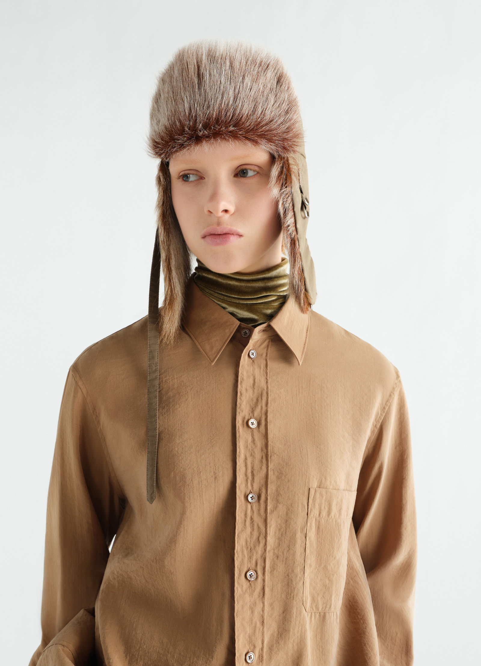 Fuzzy beige long-hair goat leather chapka by lemaire worn by model with brown shirt and green scarf