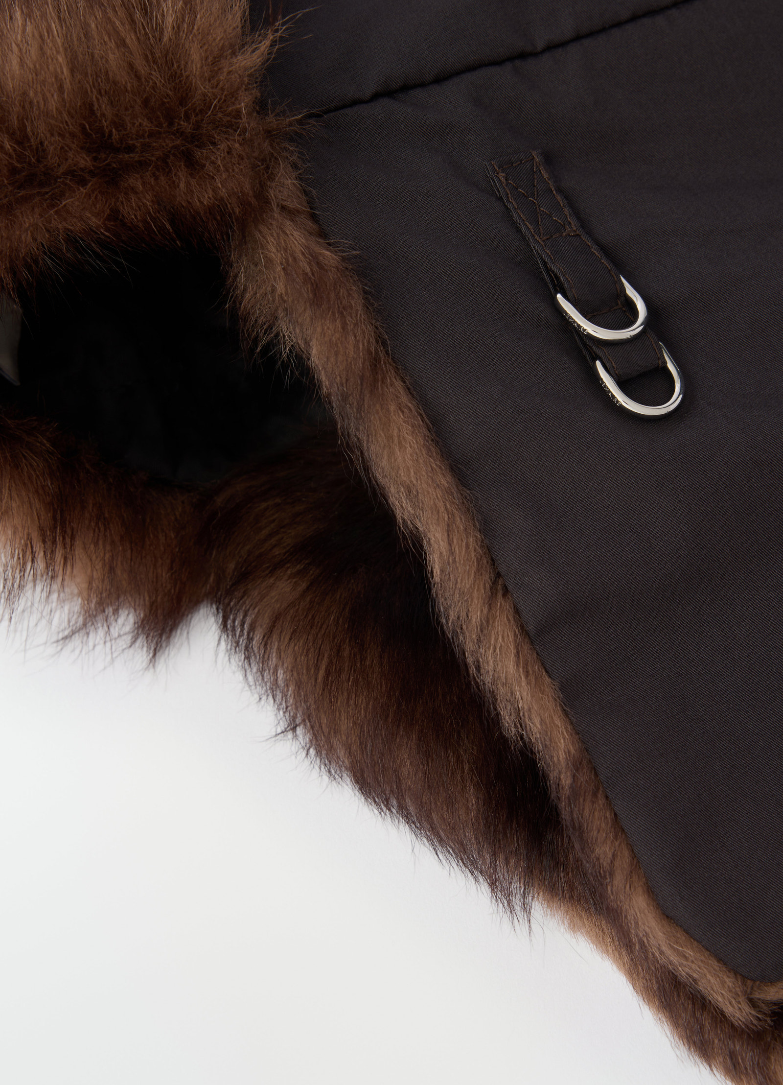 Fuzzy brown lambskin shearling chapka with silver buckles by lemaire close-up detail on white background