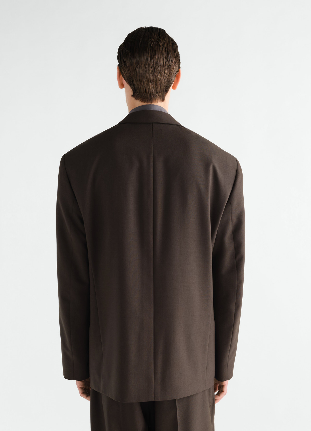 Double-breasted dark brown tropical wool blend jacket by lemaire worn by model from back view