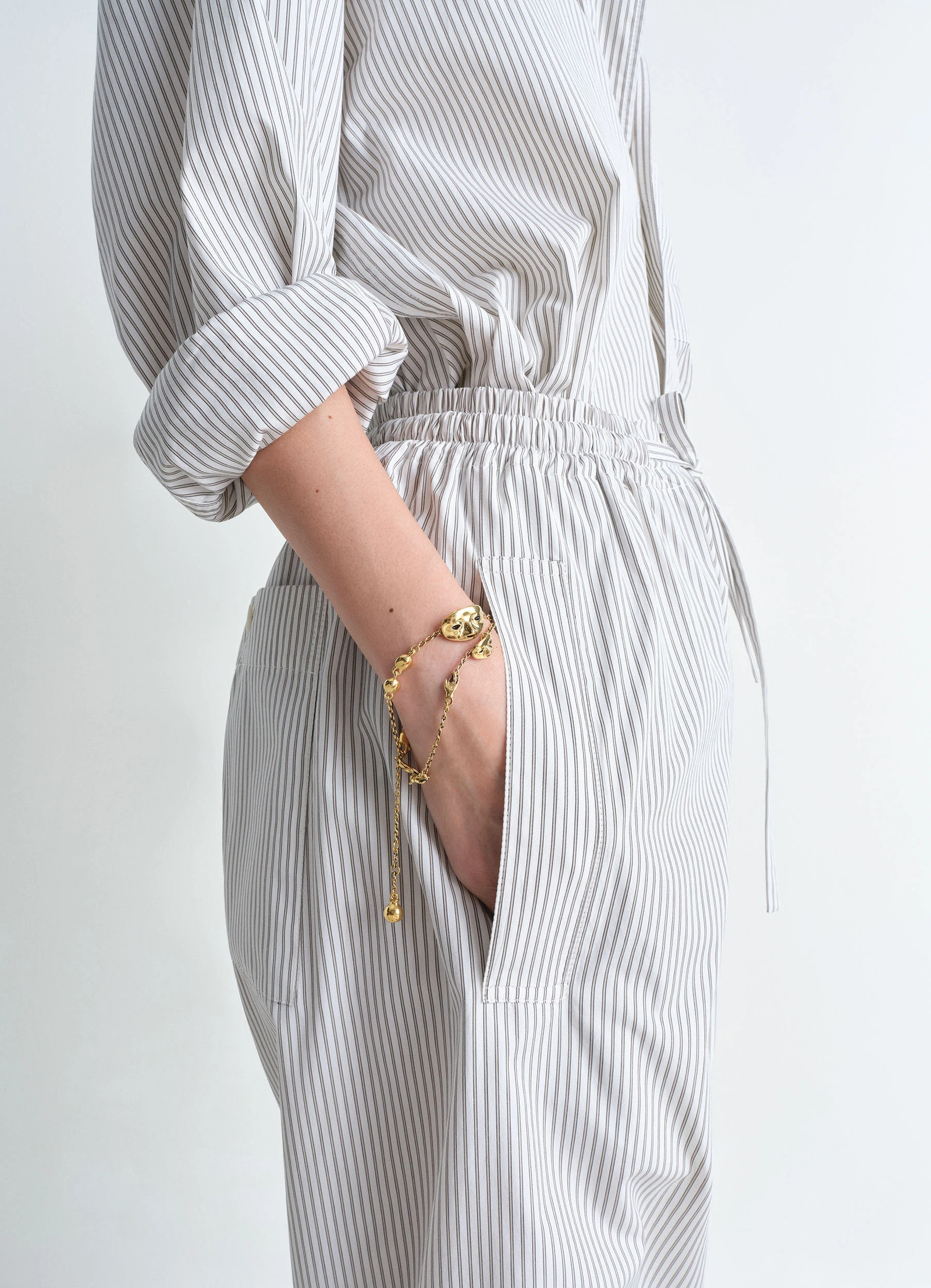Estampe bracelet in aged-effect gold-plated brass, model shot, wrist side view layered with striped outfit