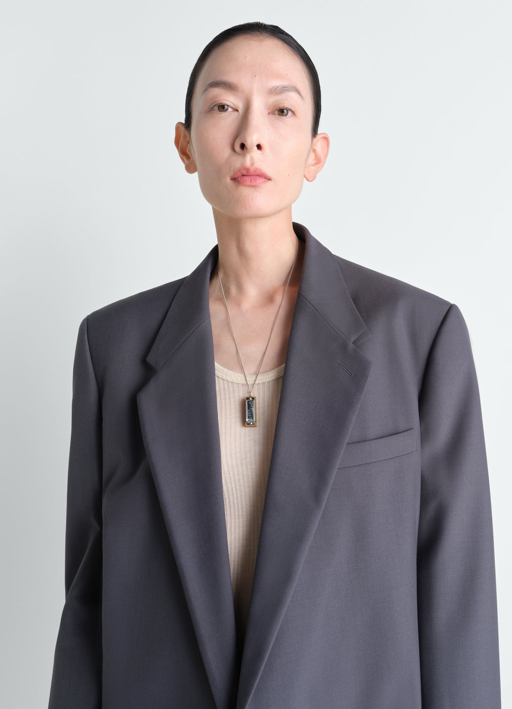 Harmonica silver-tone metal necklace worn by model LEMAIRE close-up front shot with grey blazer and beige top