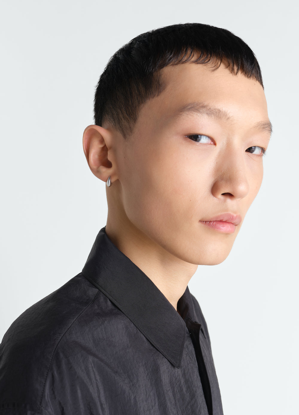 Micro drop silver earrings worn by model with black textured shirt LEMAIRE side profile close-up view.