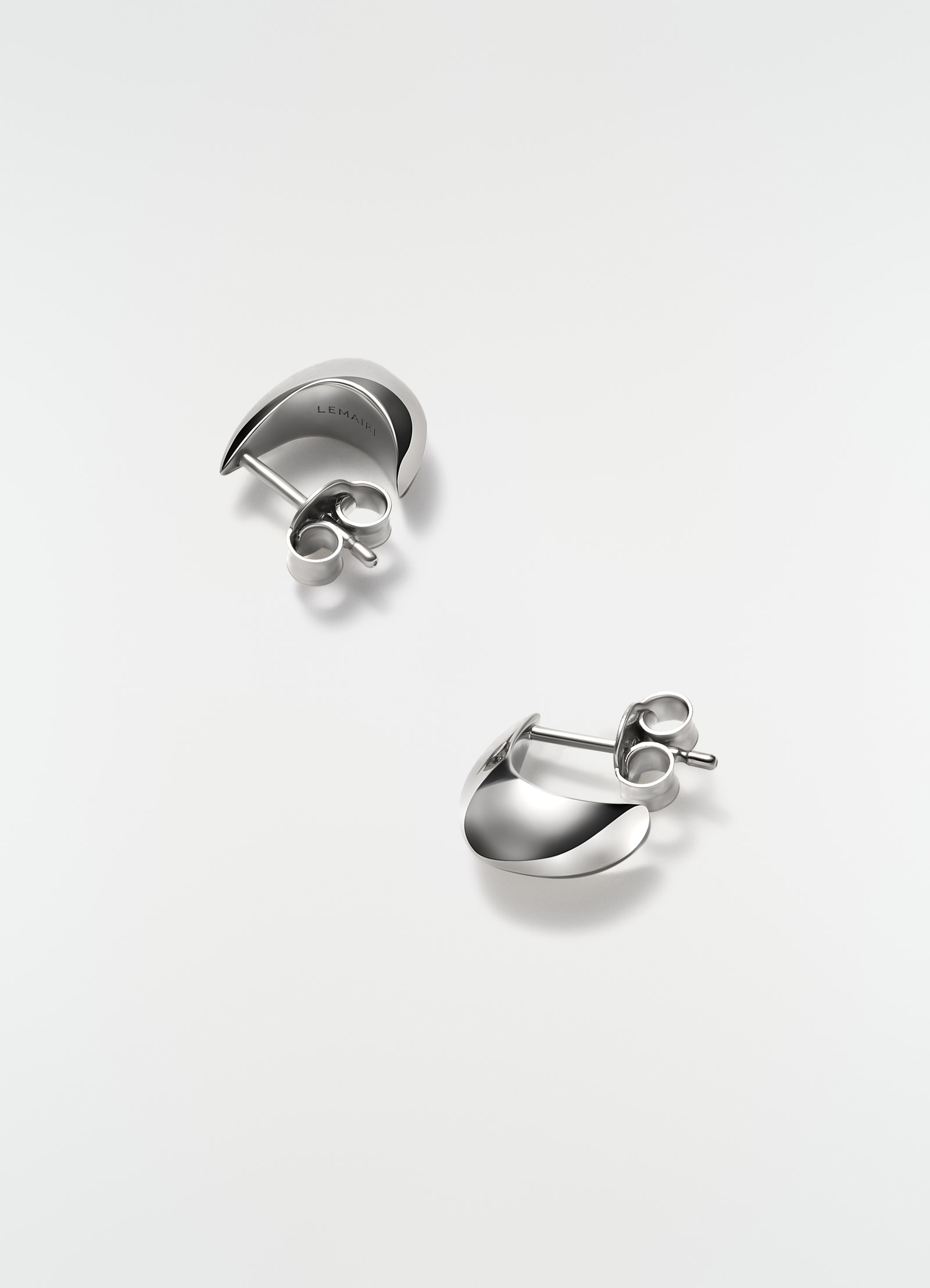 Micro silver drop earrings in polished metal by lemaire on plain white background close-up detail