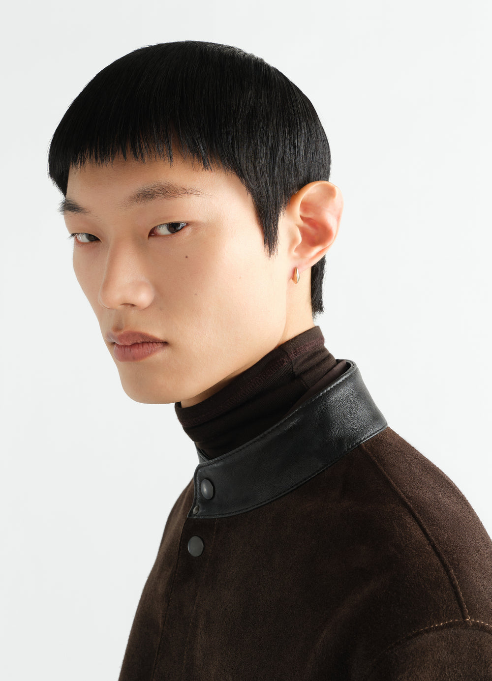 Micro Drop Earrings by LEMAIRE in gold worn by a model with brown suede jacket and leather collar close-up side view