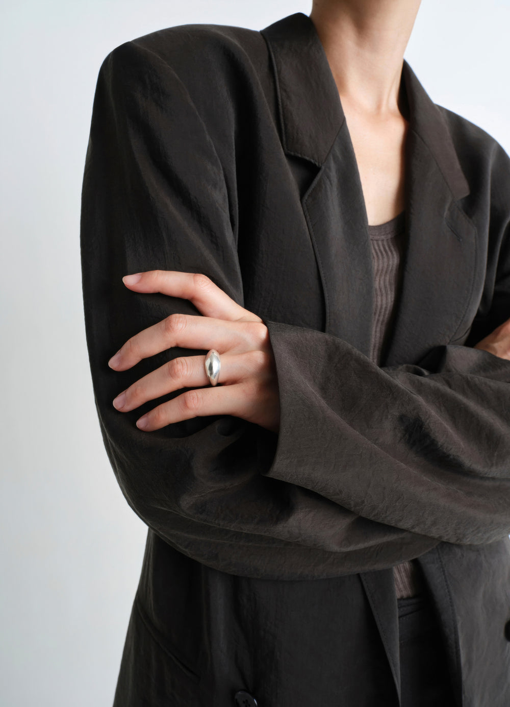 Chunky silver drop ring worn by model with black textured LEMAIRE blazer close-up detail