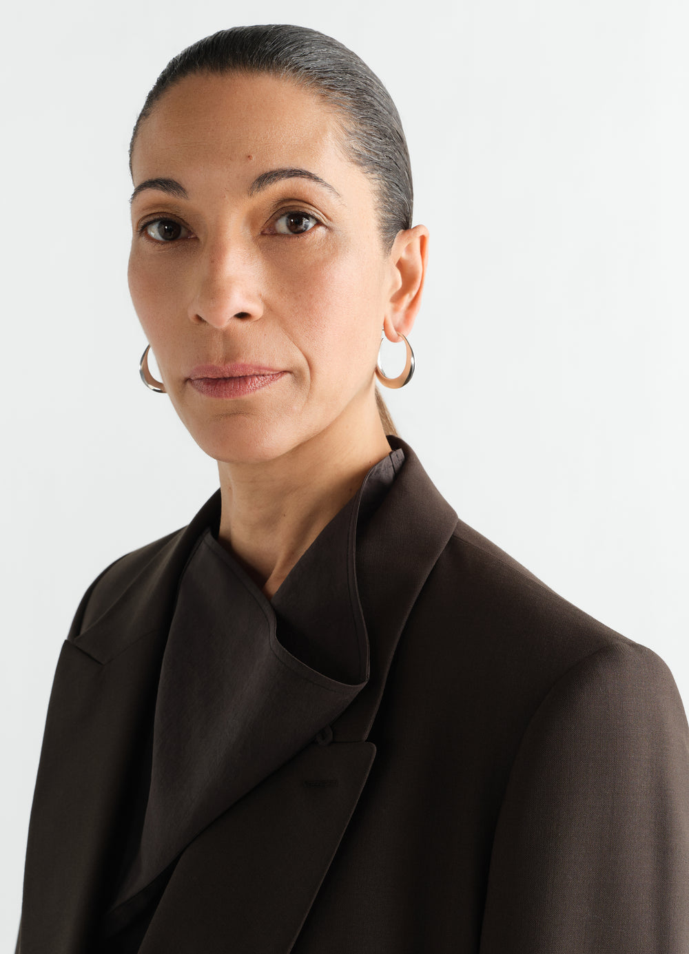 Hoops drop earrings in silver worn by a model with dark brown blazer LEMAIRE close-up front