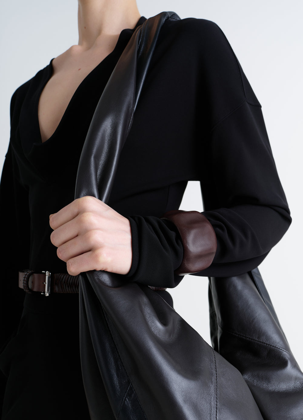 Carlos Cuff in brown leather LEMAIRE worn by model with black outfit and leather bag close-up detail