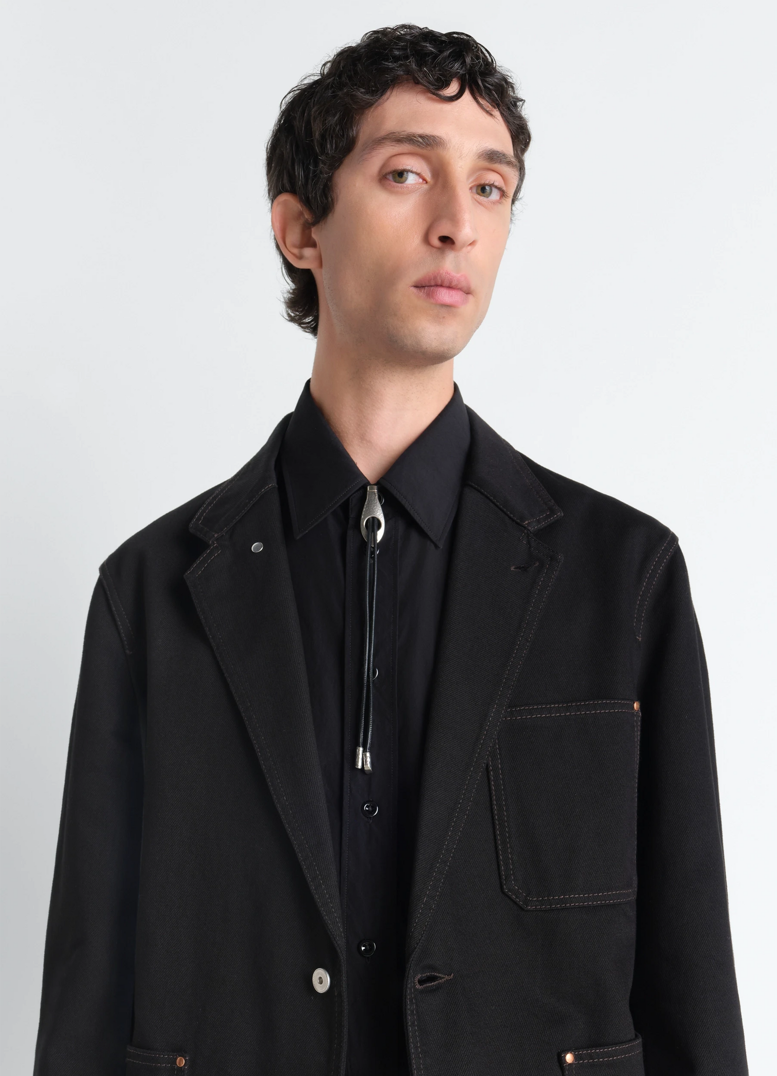 Snake bolo tie necklace in leather and brass, model shot, three-quarter view worn under jacket