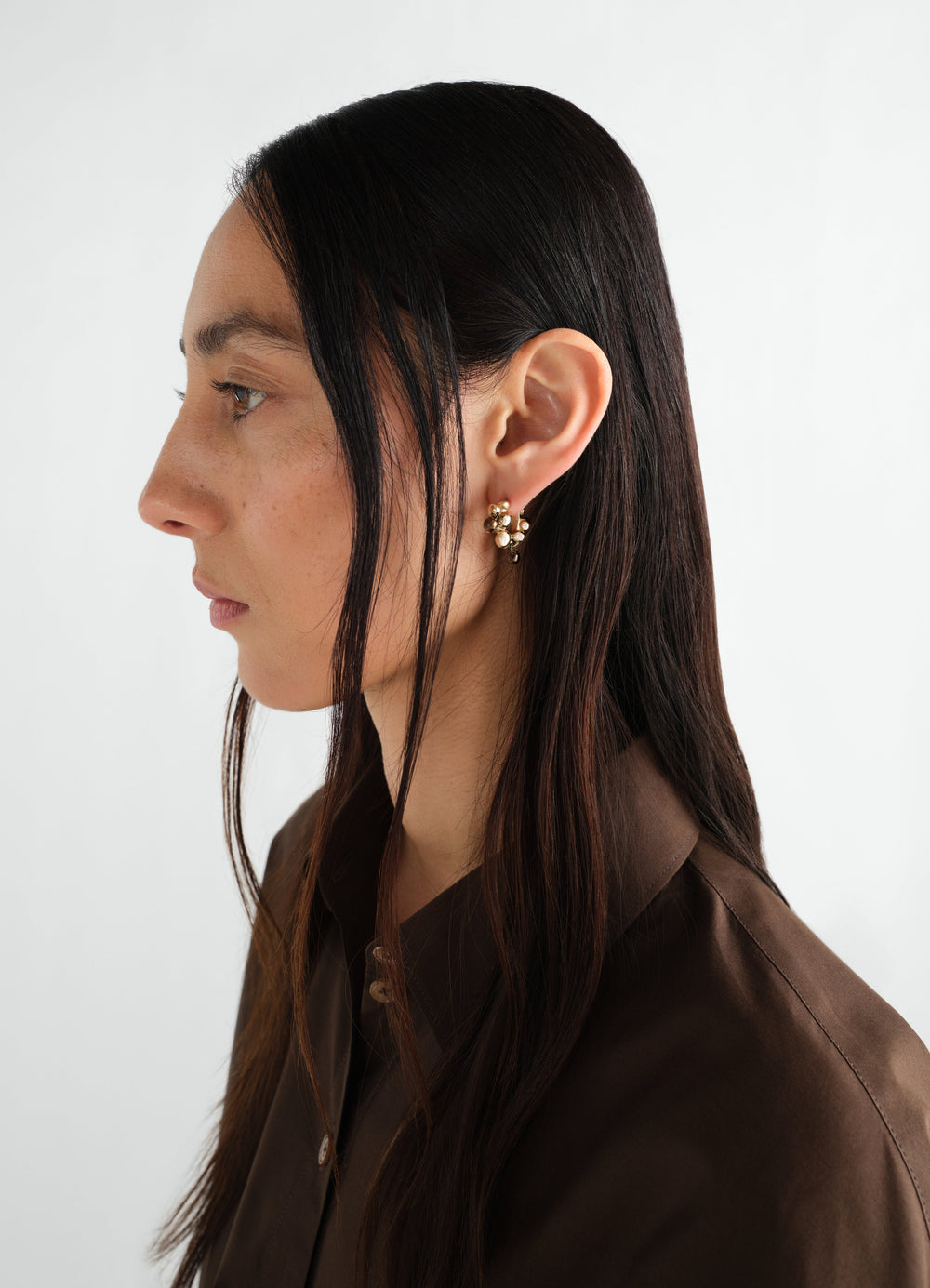 Seeds hoop earrings in gold-tone brass LEMAIRE worn by a model side profile with brown shirt