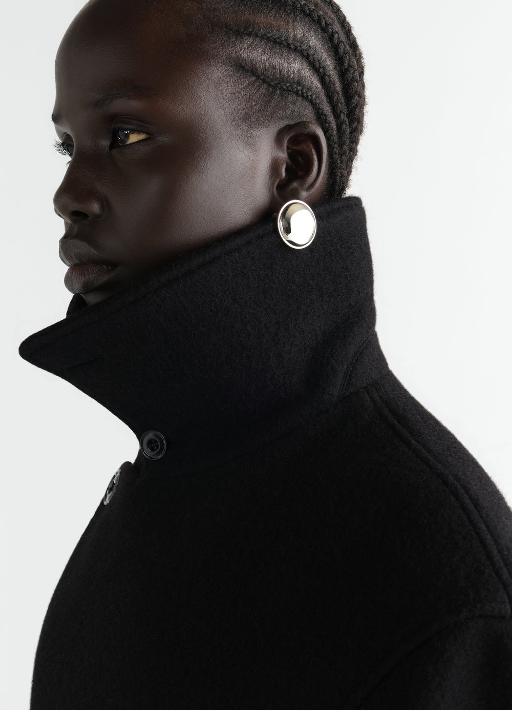 Witch Mirror brass earrings worn by model with black wool coat high collar LEMAIRE side view
