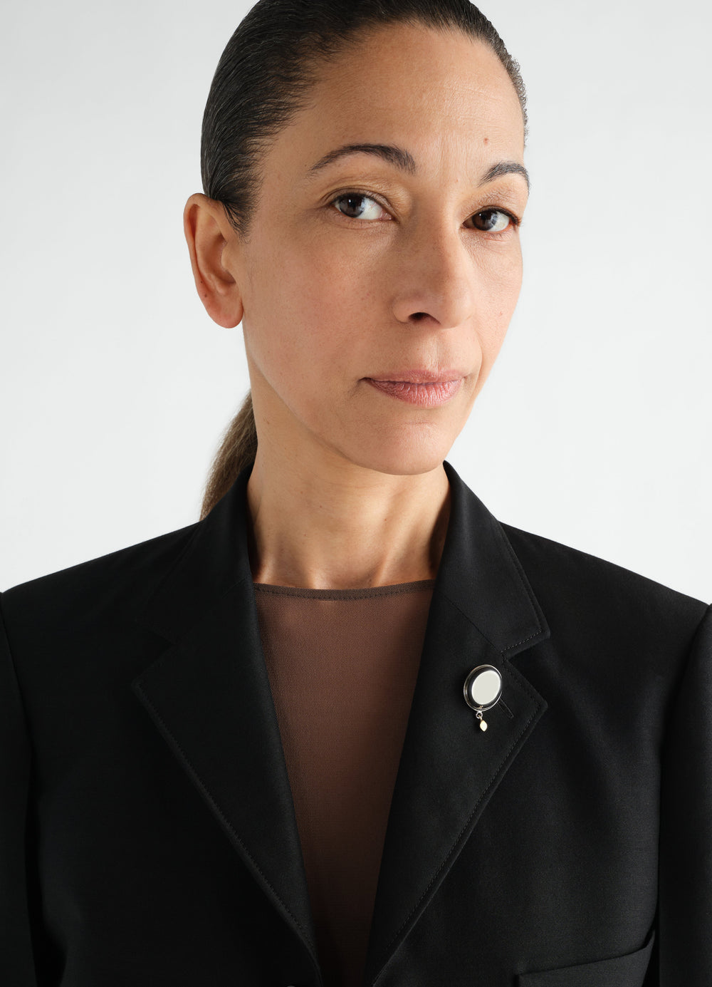 Witch Mirror brass pin in silver and pearl detail worn by model on black LEMAIRE blazer front close-up