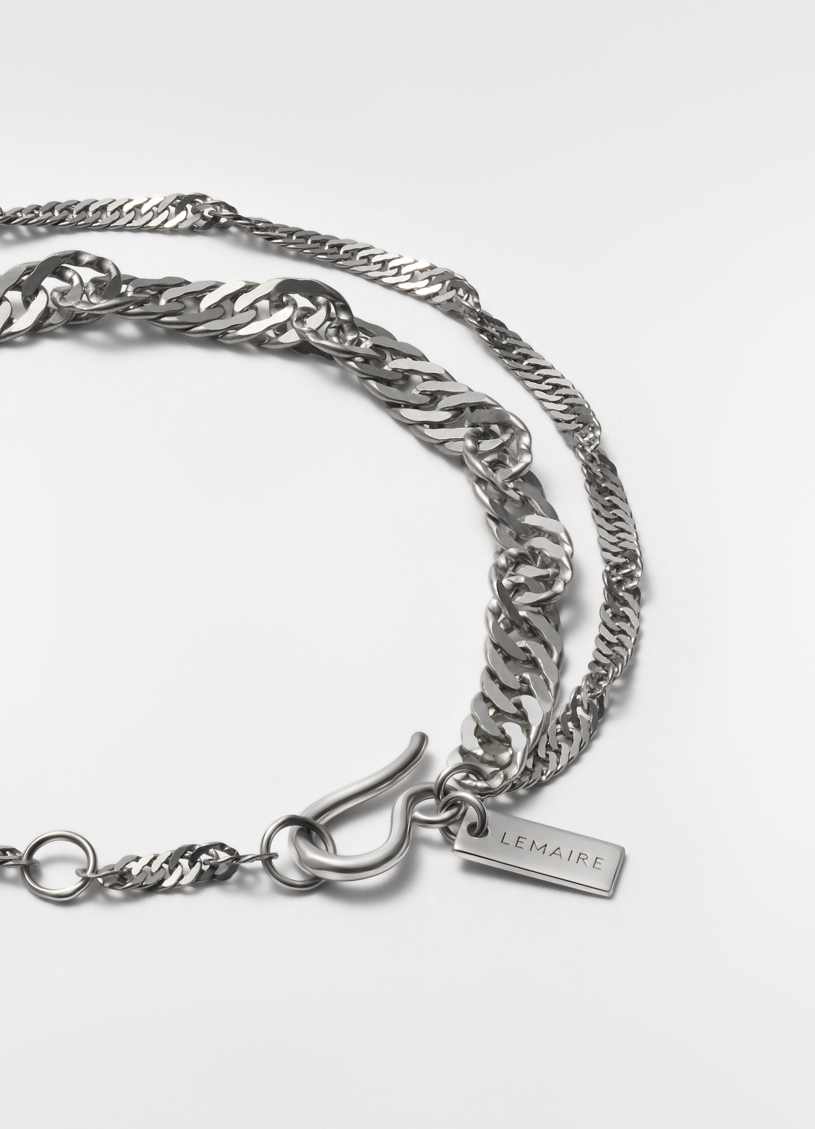 Twisted rhodium-plated silver chain bracelet by lemaire with engraved tag close-up on white background