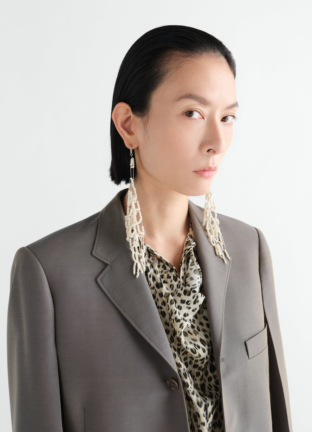 Glass bead tassel earrings in white worn by model with brown blazer and animal print top LEMAIRE close-up front