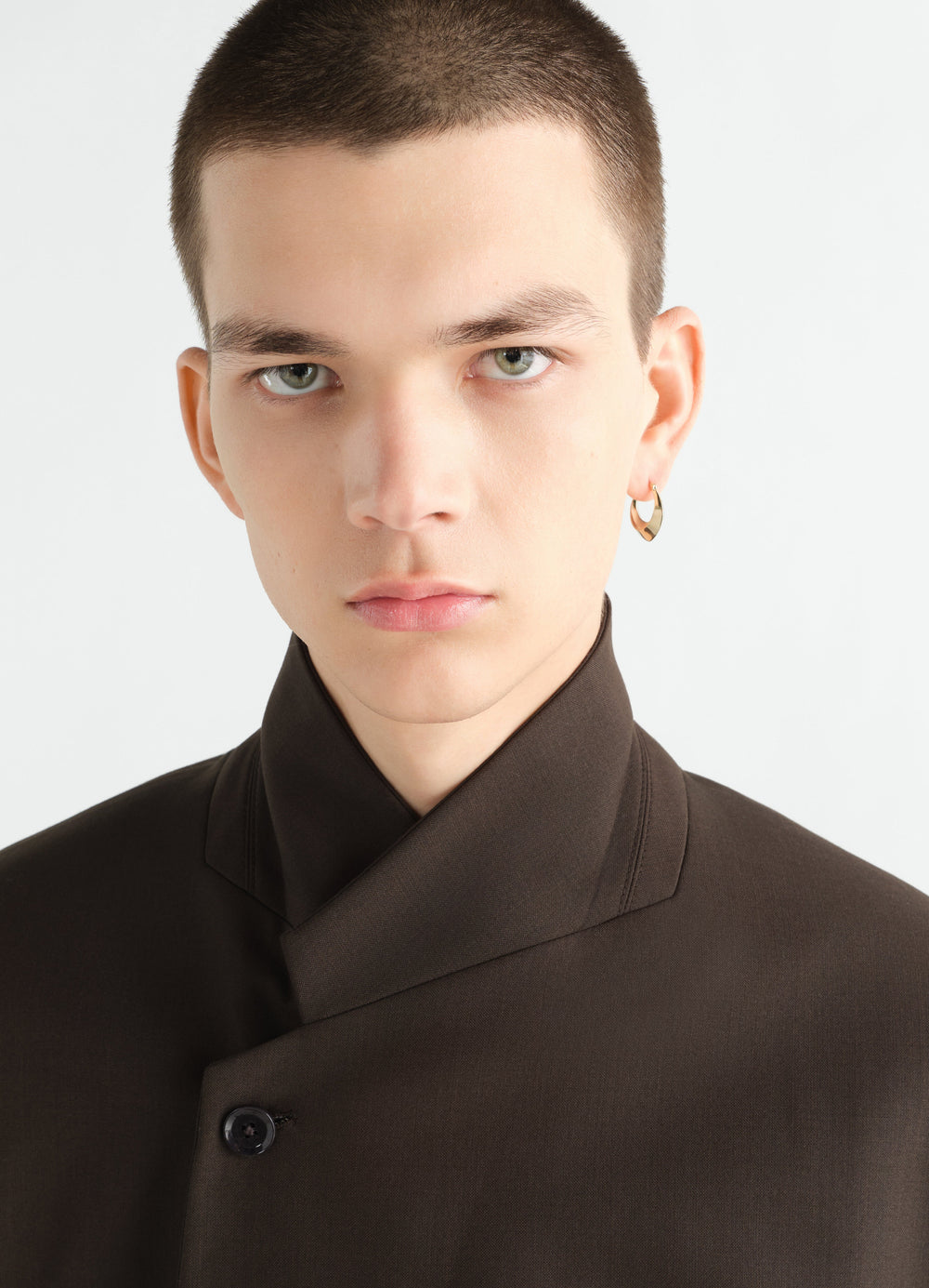 Drop edge hoop earrings gold-plated silver by LEMAIRE worn by model close-up front view with brown jacket