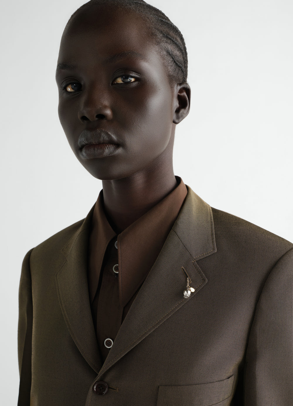 Thistle buttonhole ornament in brass by LEMAIRE worn on brown suit lapel close-up on model