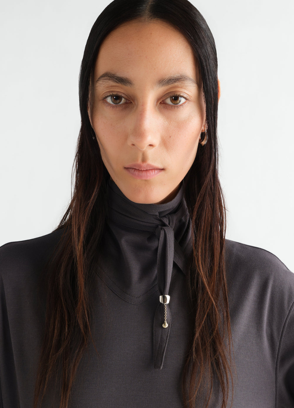 Scarf ornament in brass by LEMAIRE worn by model with tied dark grey fabric detail close-up front view