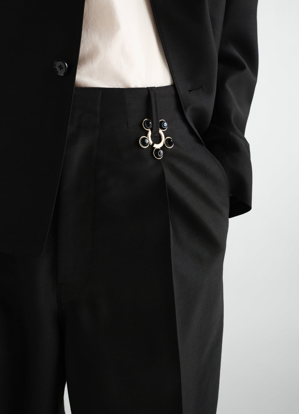 Garment ornament necklace brass with black details worn on black trousers by model LEMAIRE close-up front