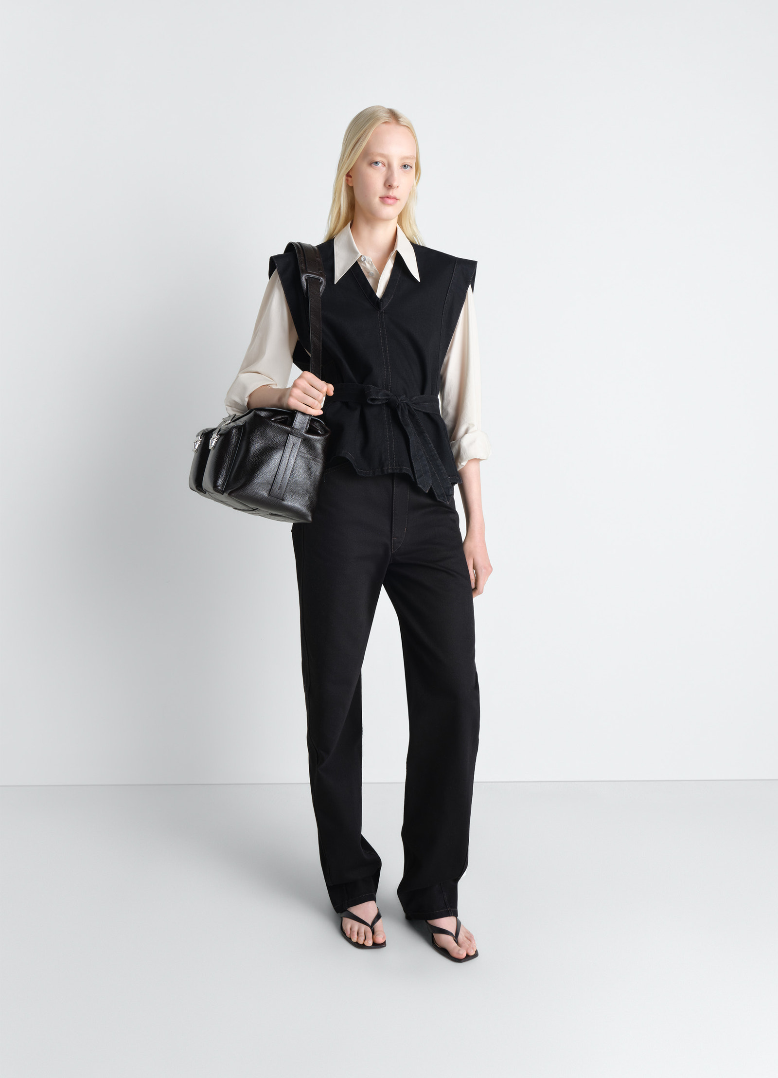 Lemaire chasuble in deep black denim, model shot, three-quarter view peplum hem detail