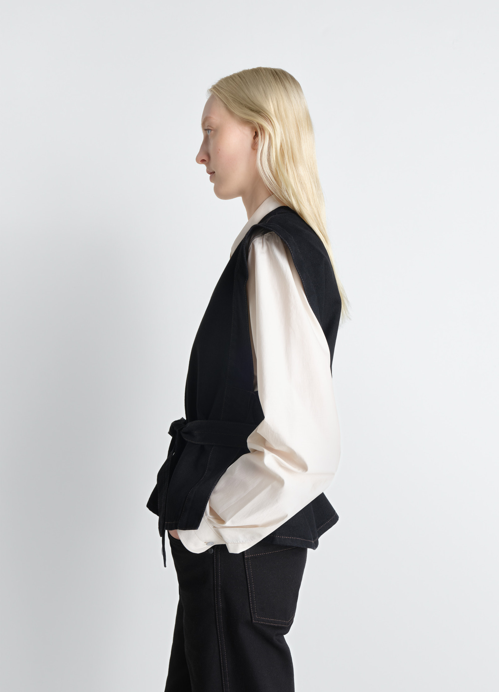 Lemaire chasuble in deep black denim, model shot, side profile view belted waist