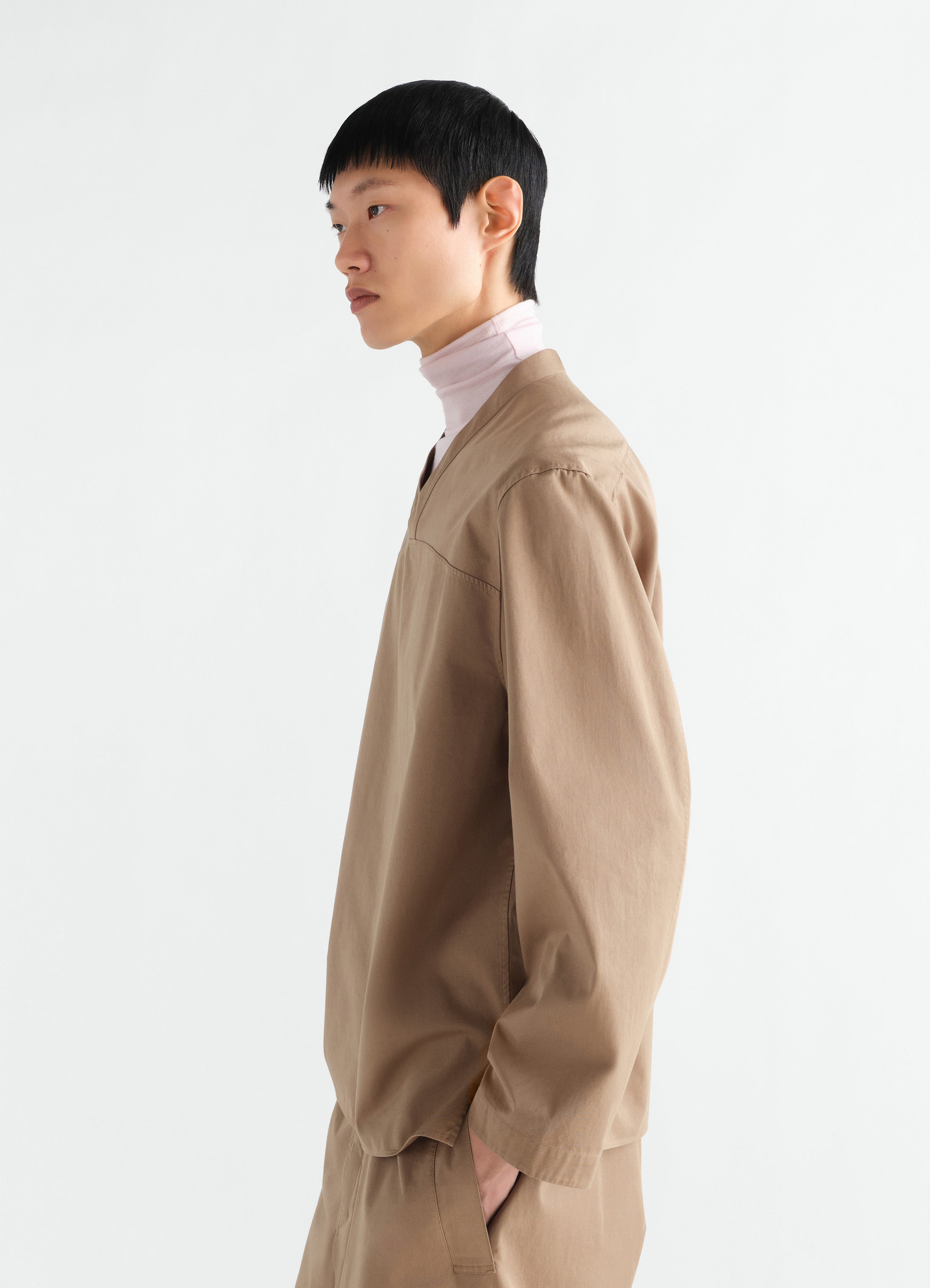 V-neck top lemaire light brown cotton twill side view worn by model with pink turtleneck