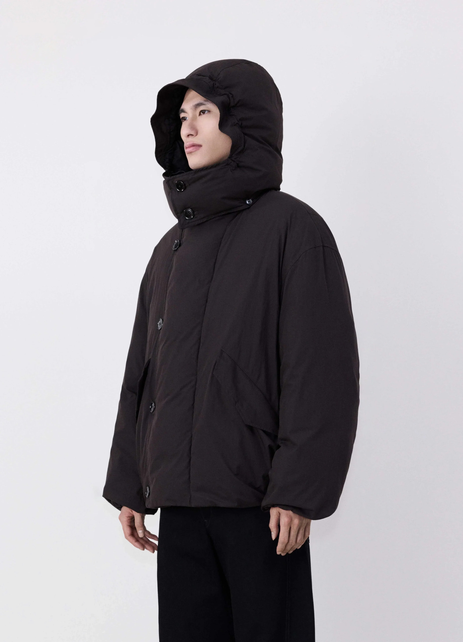 Lemaire hooded puffer blouson in dark cotton blend, model shot, side three-quarter view padded quilted fabric